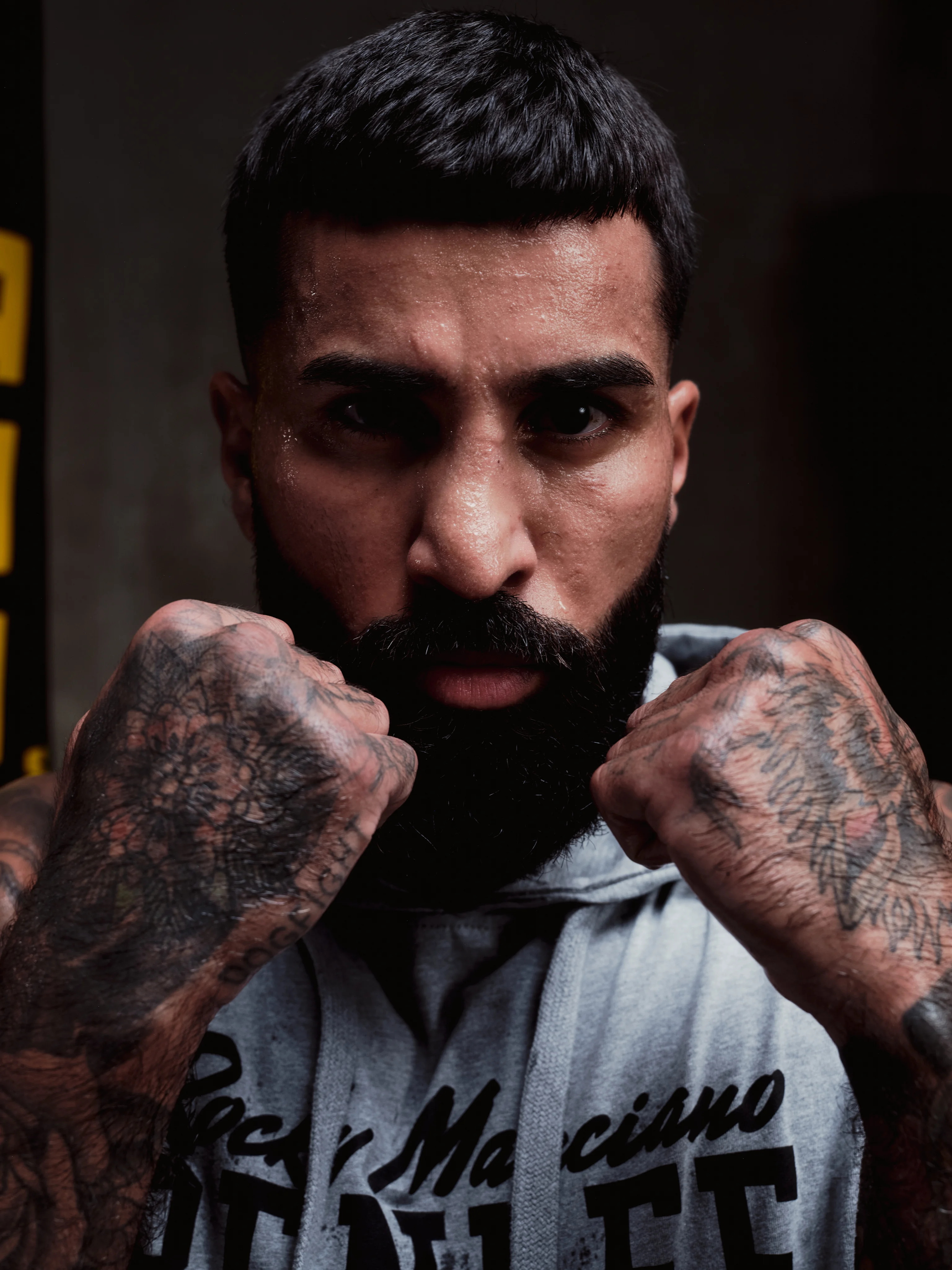 Tattooed boxer with raised fists in a grey BENLEE hoodie