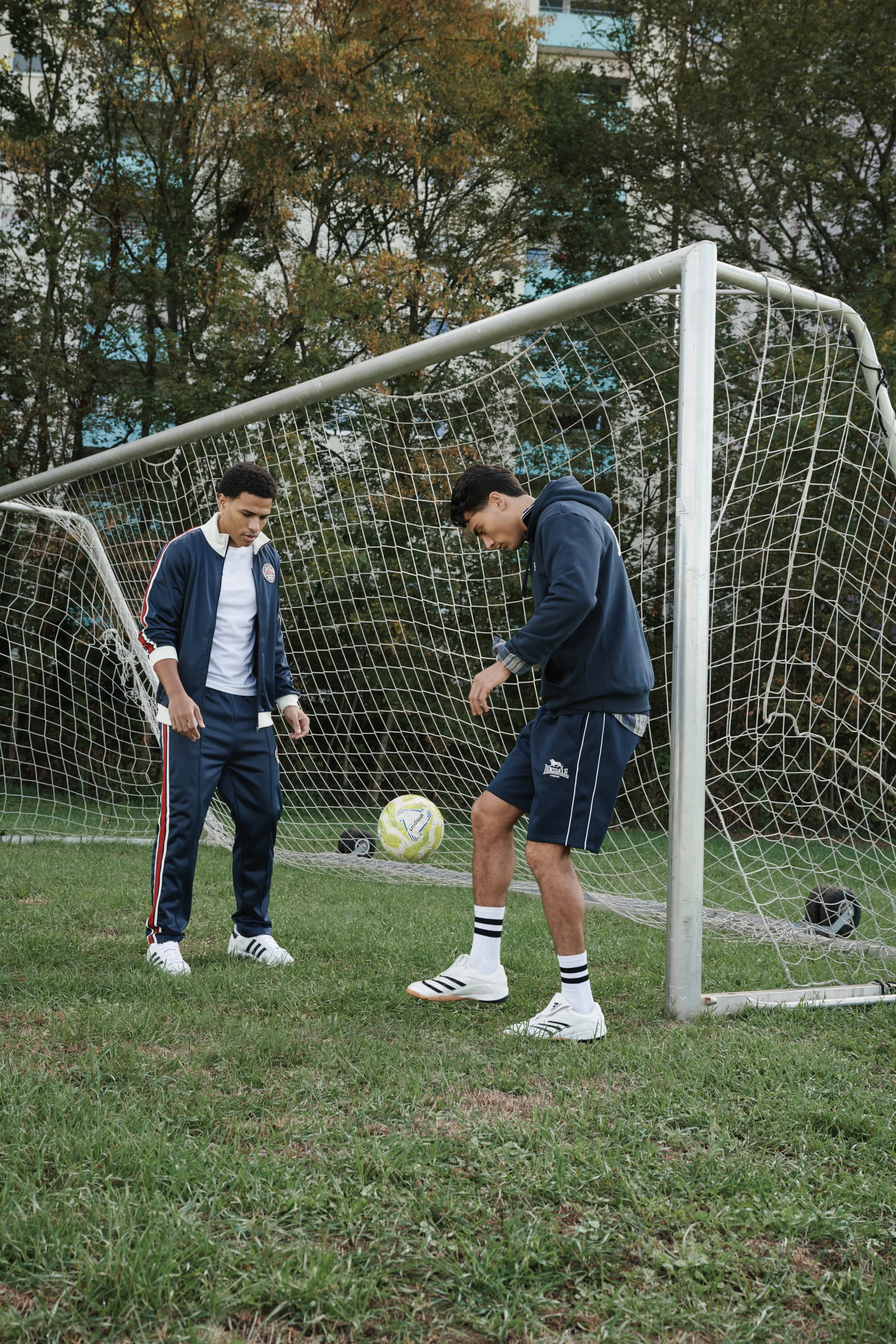 Two men playing football in front of a goal on a grass pitch