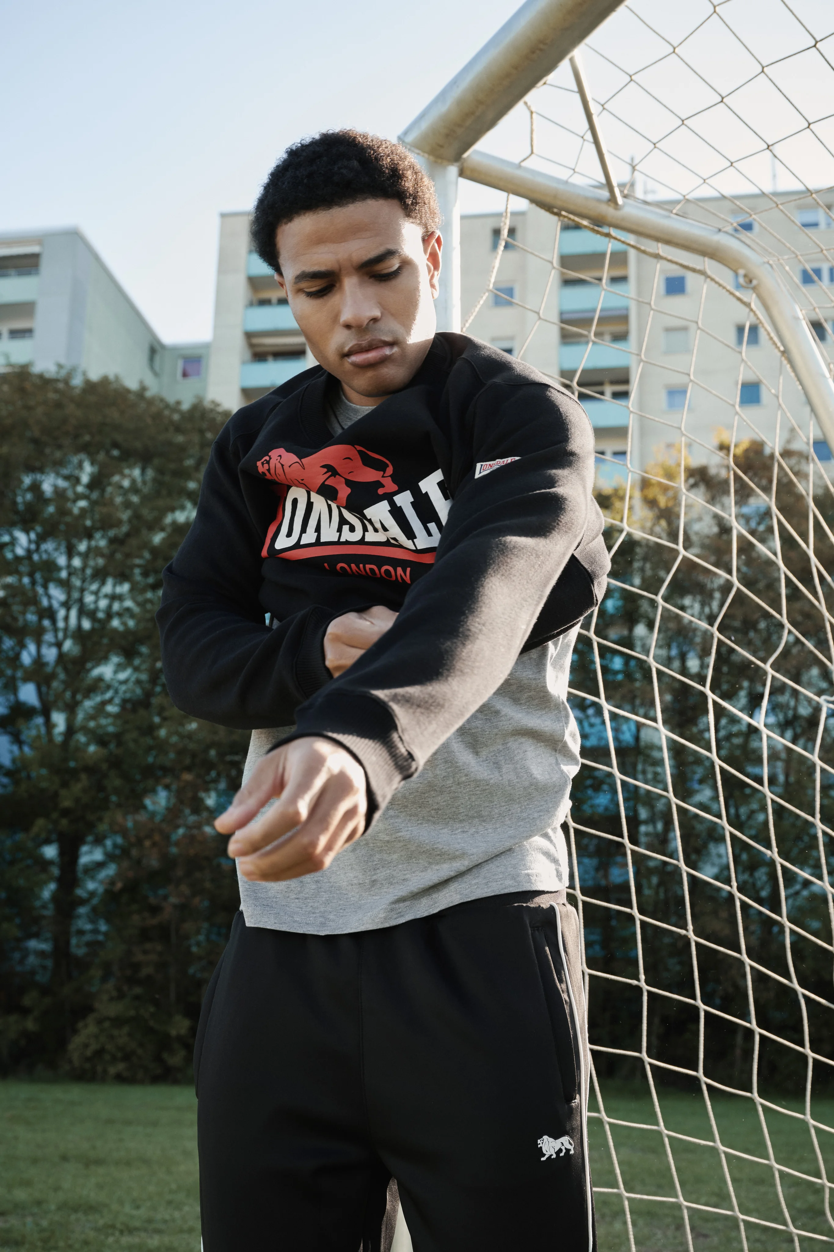 Man in a black Lonsdale hoodie with a red logo in front of a goal net