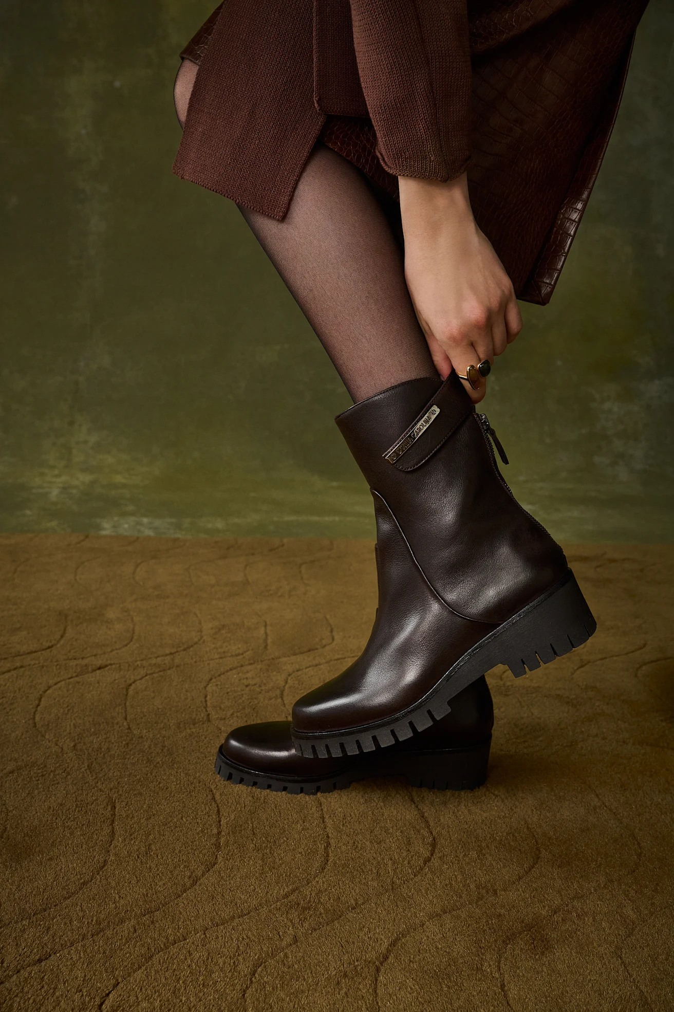 Model pulling on a dark brown leather ankle boot with a lug sole