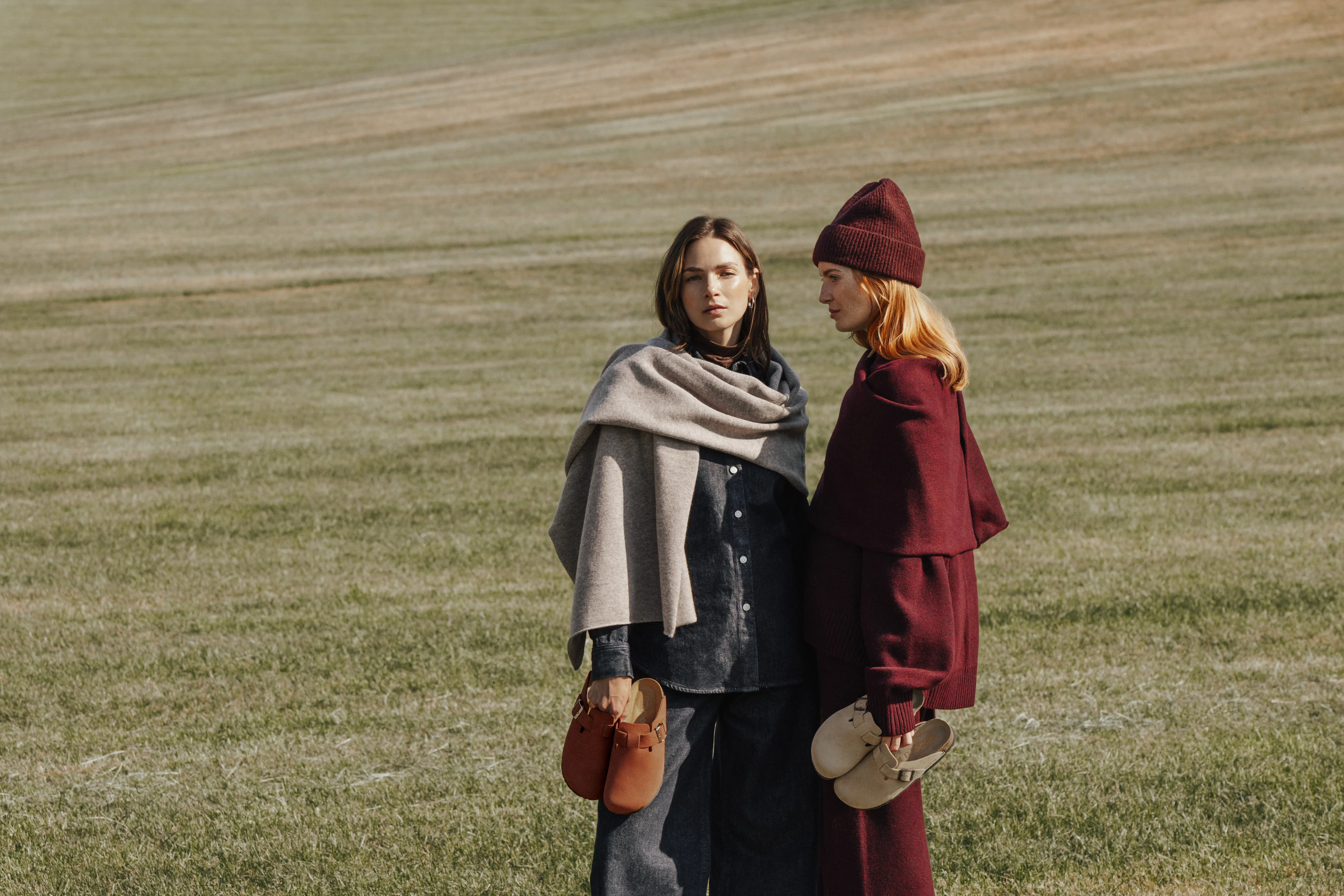 Two models in coats and scarves standing in a field