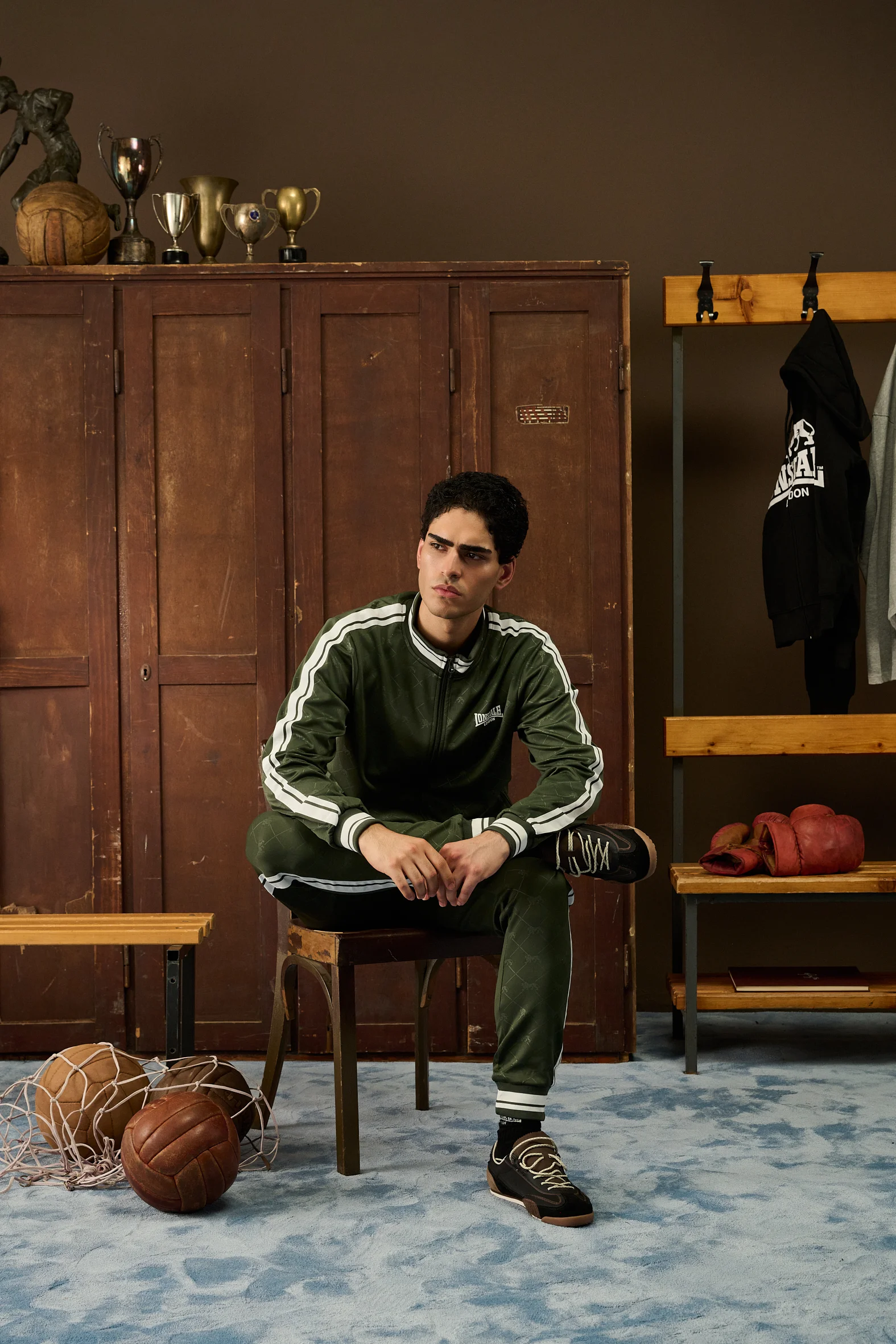 Man in a green Lonsdale tracksuit sitting on a stool in the locker room