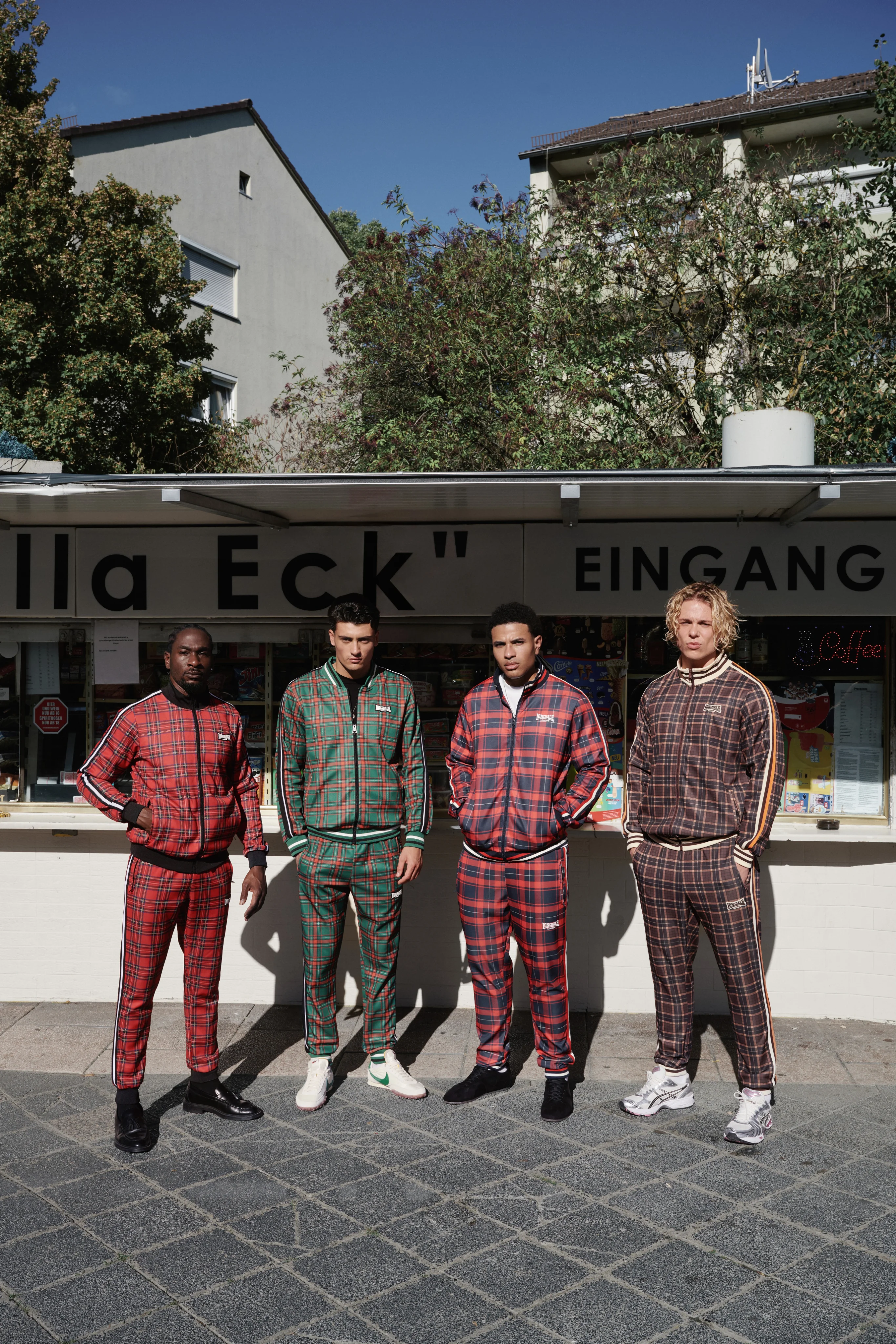Four men in checked tracksuits lined up in front of a kiosk