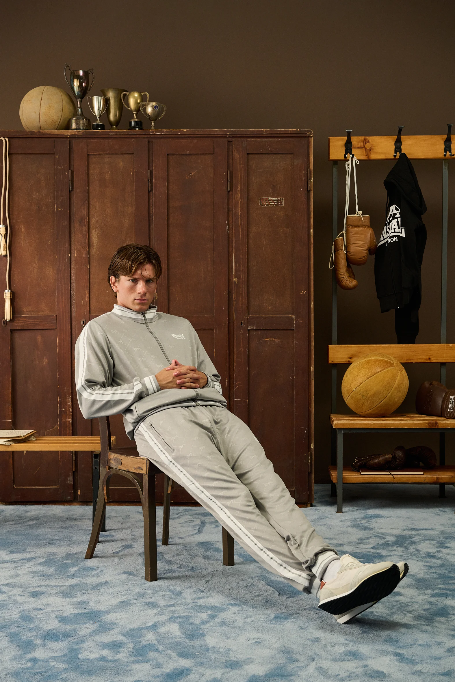 Man in a grey Lonsdale tracksuit leaning back on a chair in the locker room
