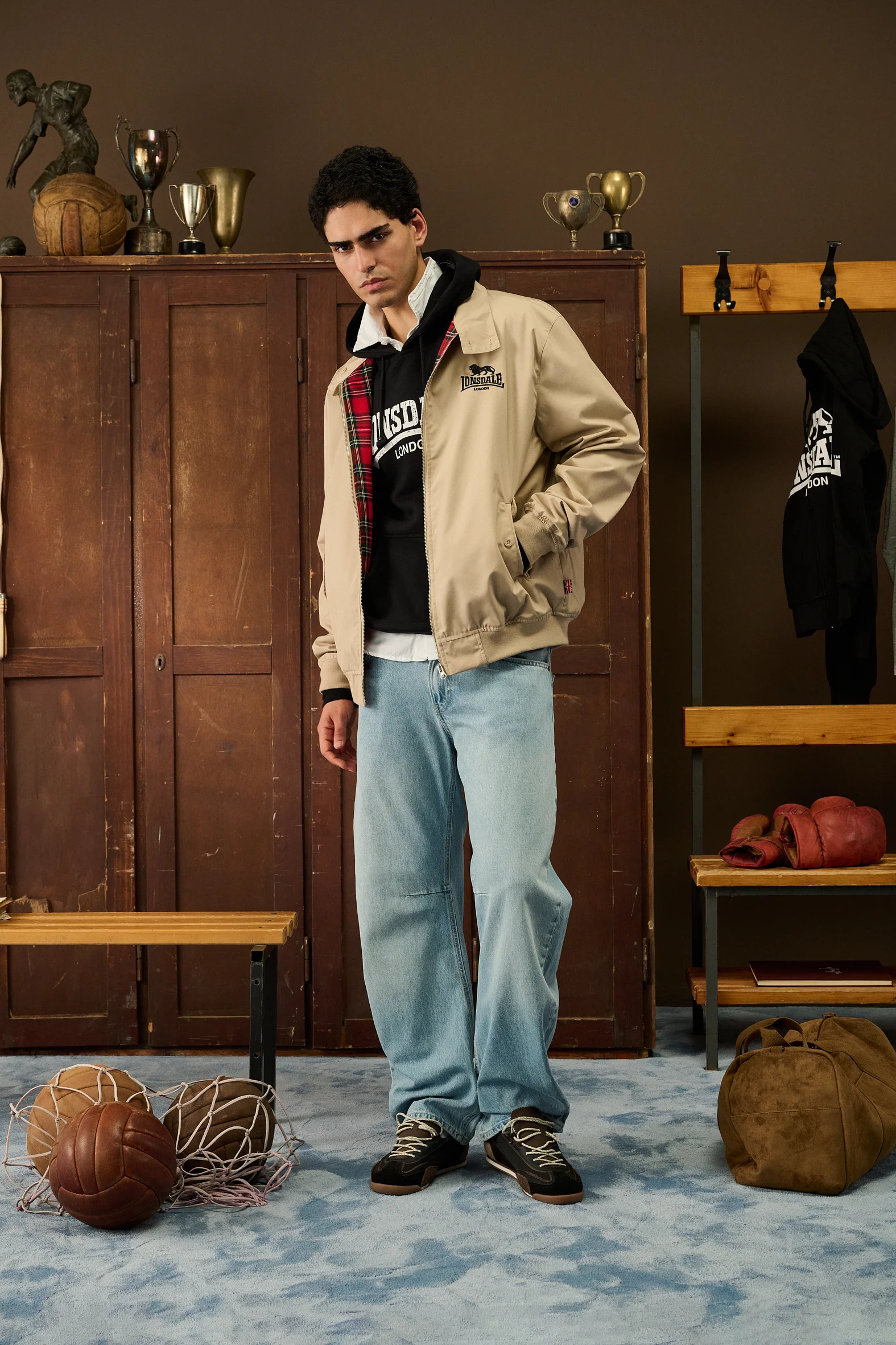 Man in a beige Lonsdale jacket and light jeans next to old leather balls