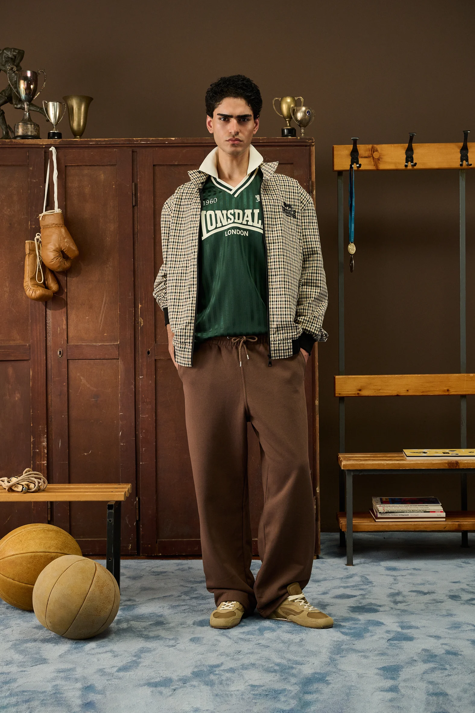 Man in a checked jacket over a green Lonsdale shirt and brown trousers