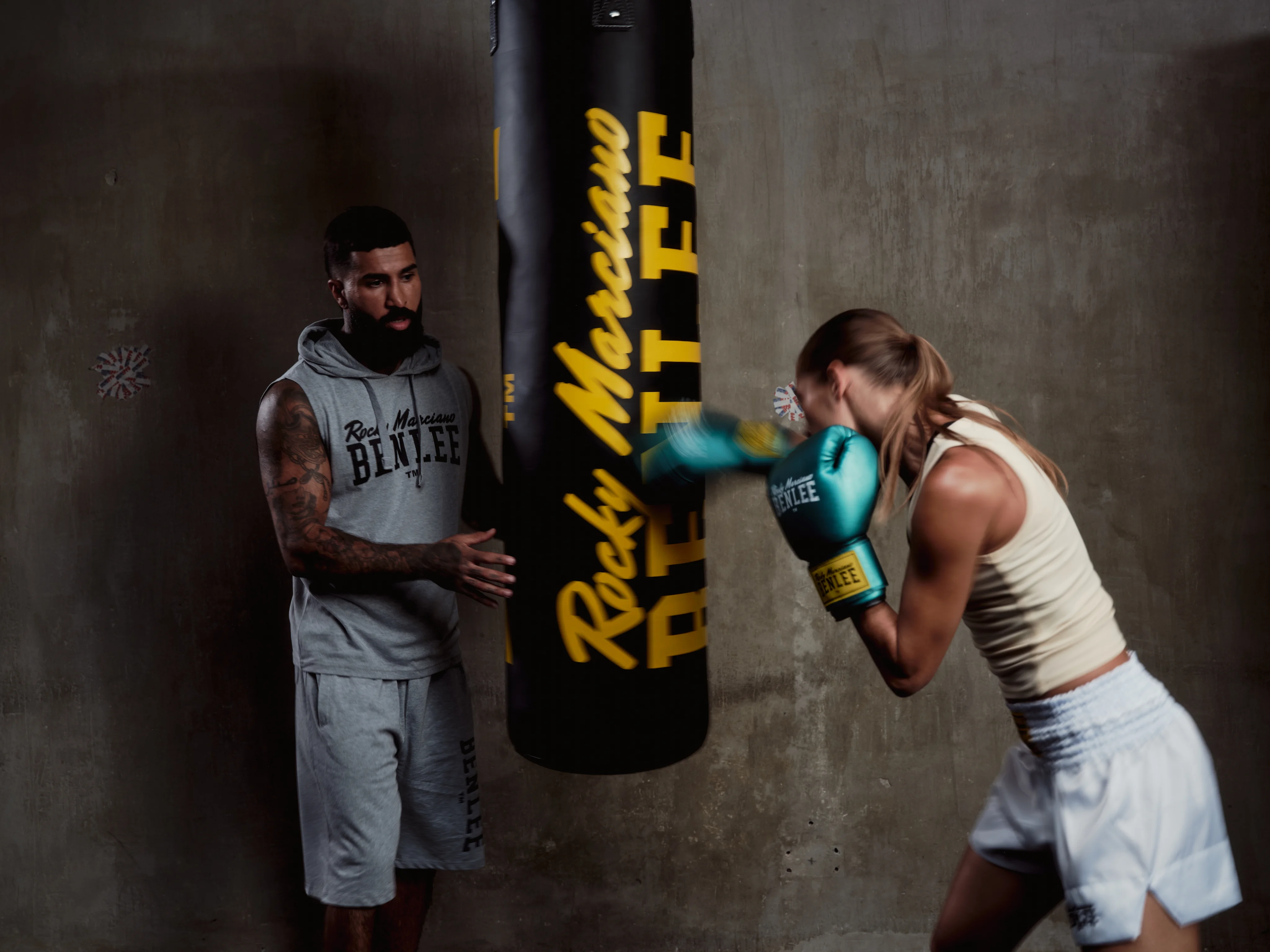Boxer hitting a heavy bag, her coach beside her