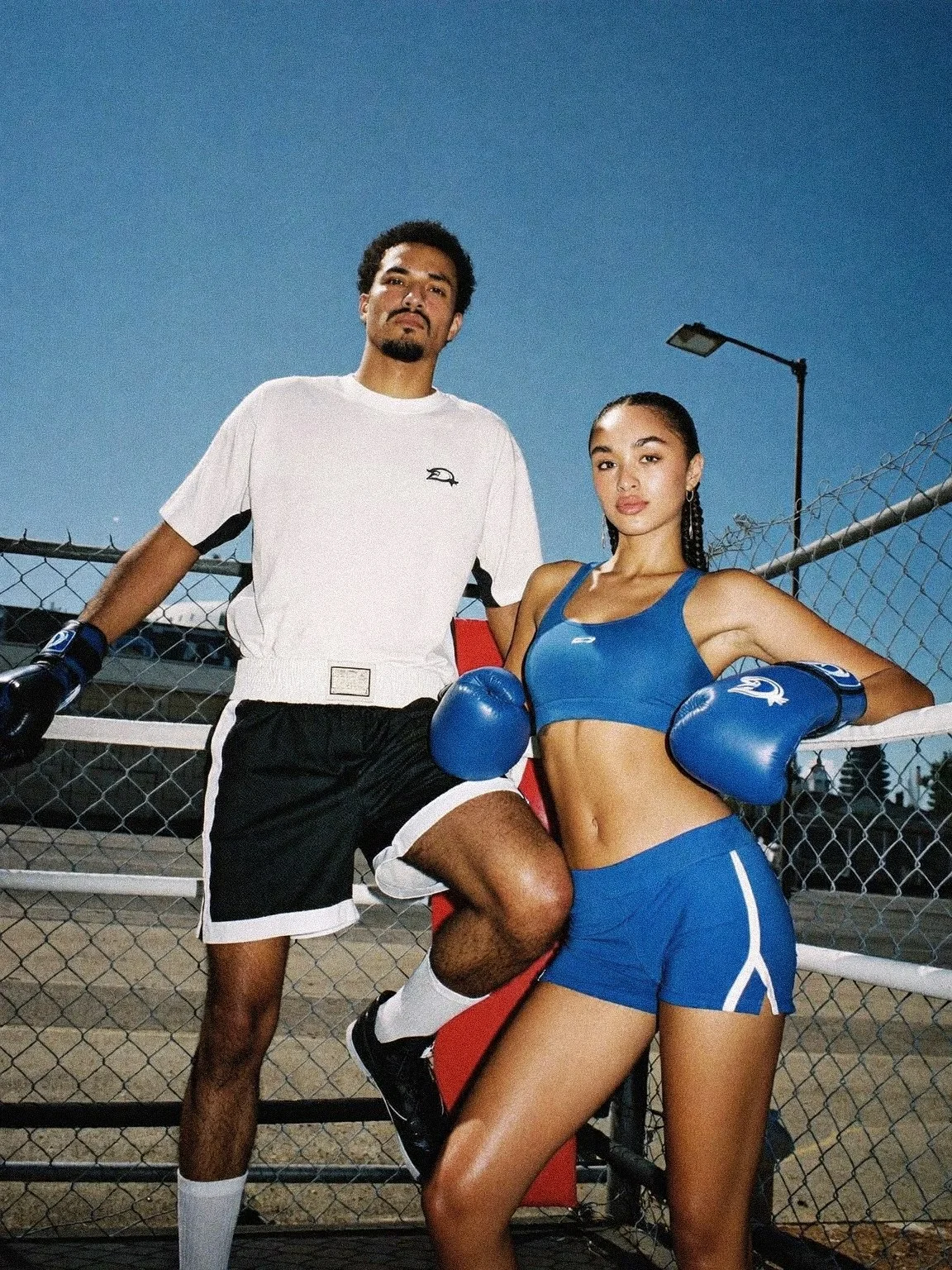 Two athletes with boxing gloves in front of a fence