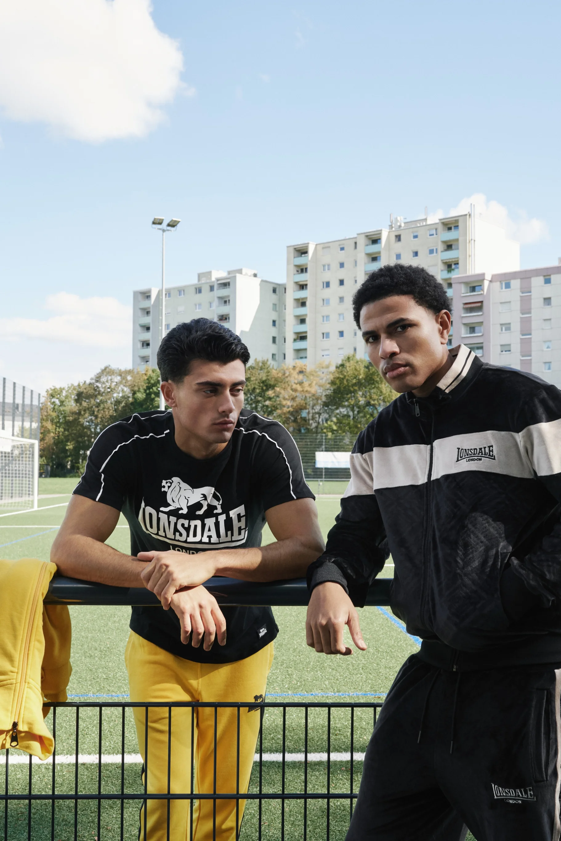 Two men leaning on the railing of a football pitch