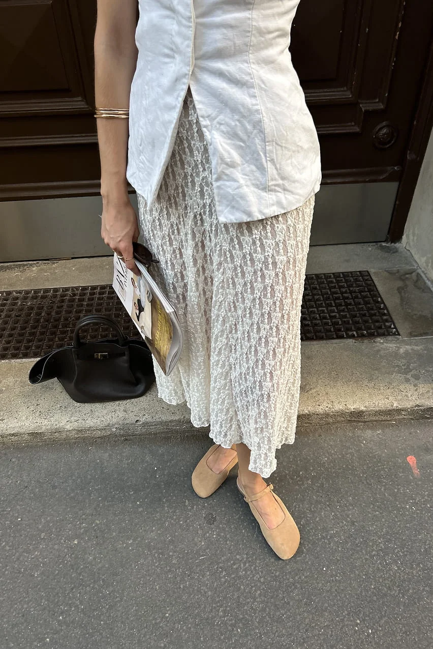 Woman in a white lace skirt with a black bag and a magazine.