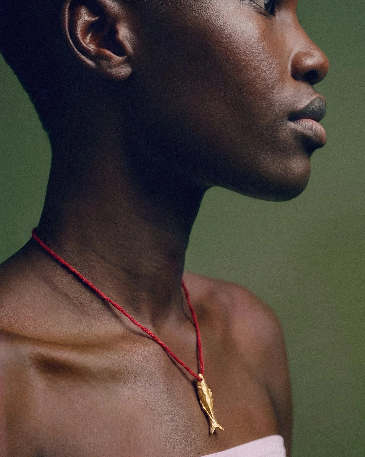 Model in profile wearing a gold fish pendant on a red cord