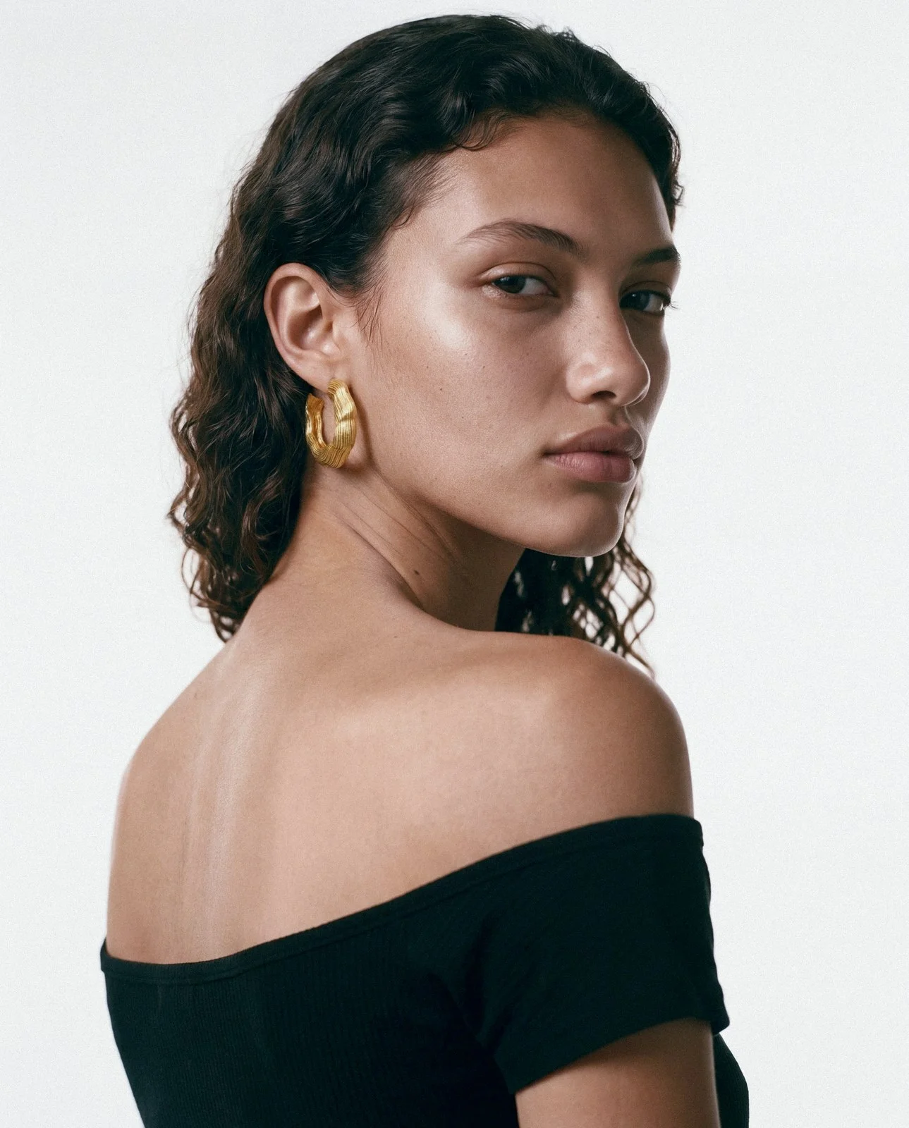 Model with a gold ear cuff in a black off-shoulder top