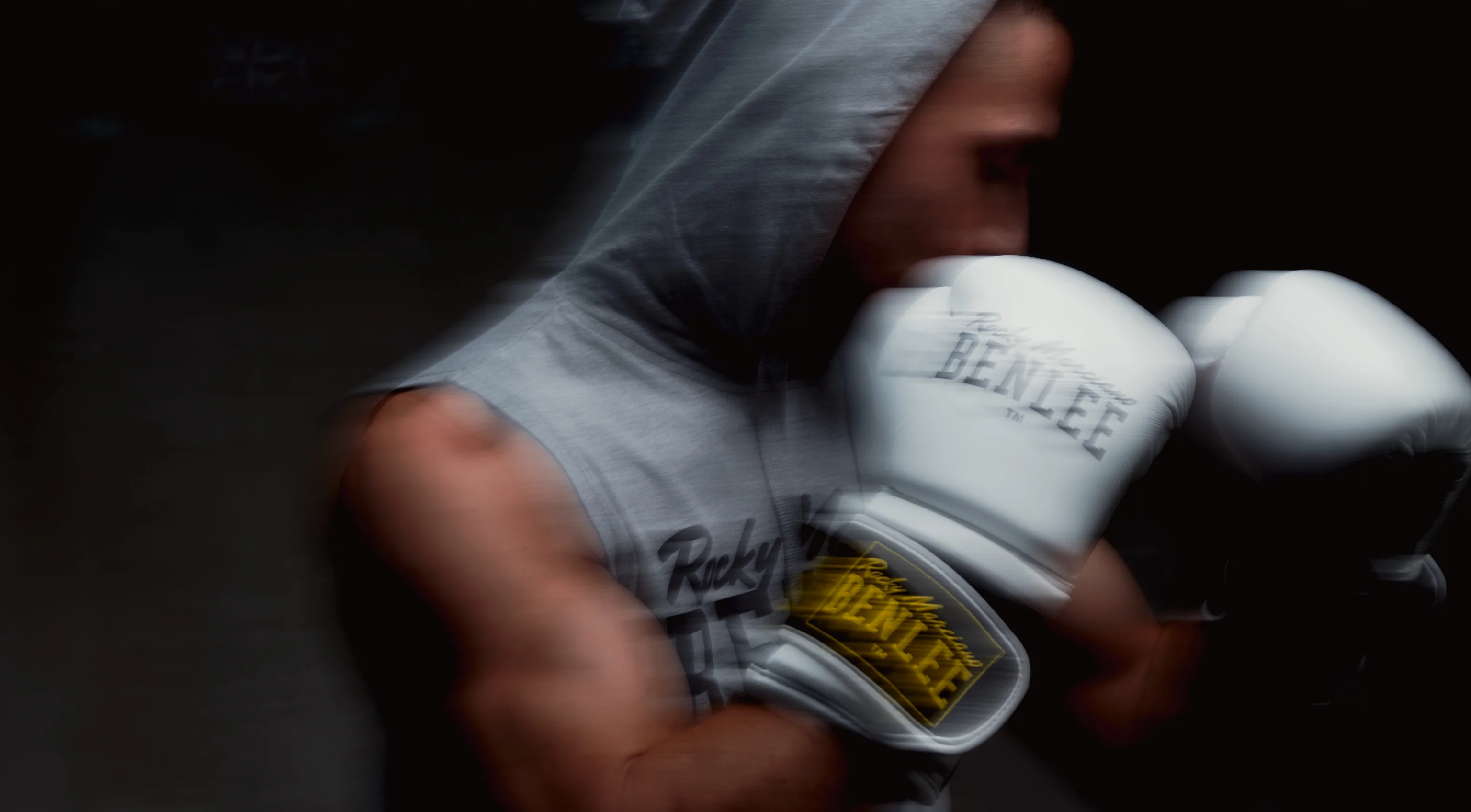 Boxer in a grey sleeveless hoodie and white BENLEE gloves, in motion against a dark background