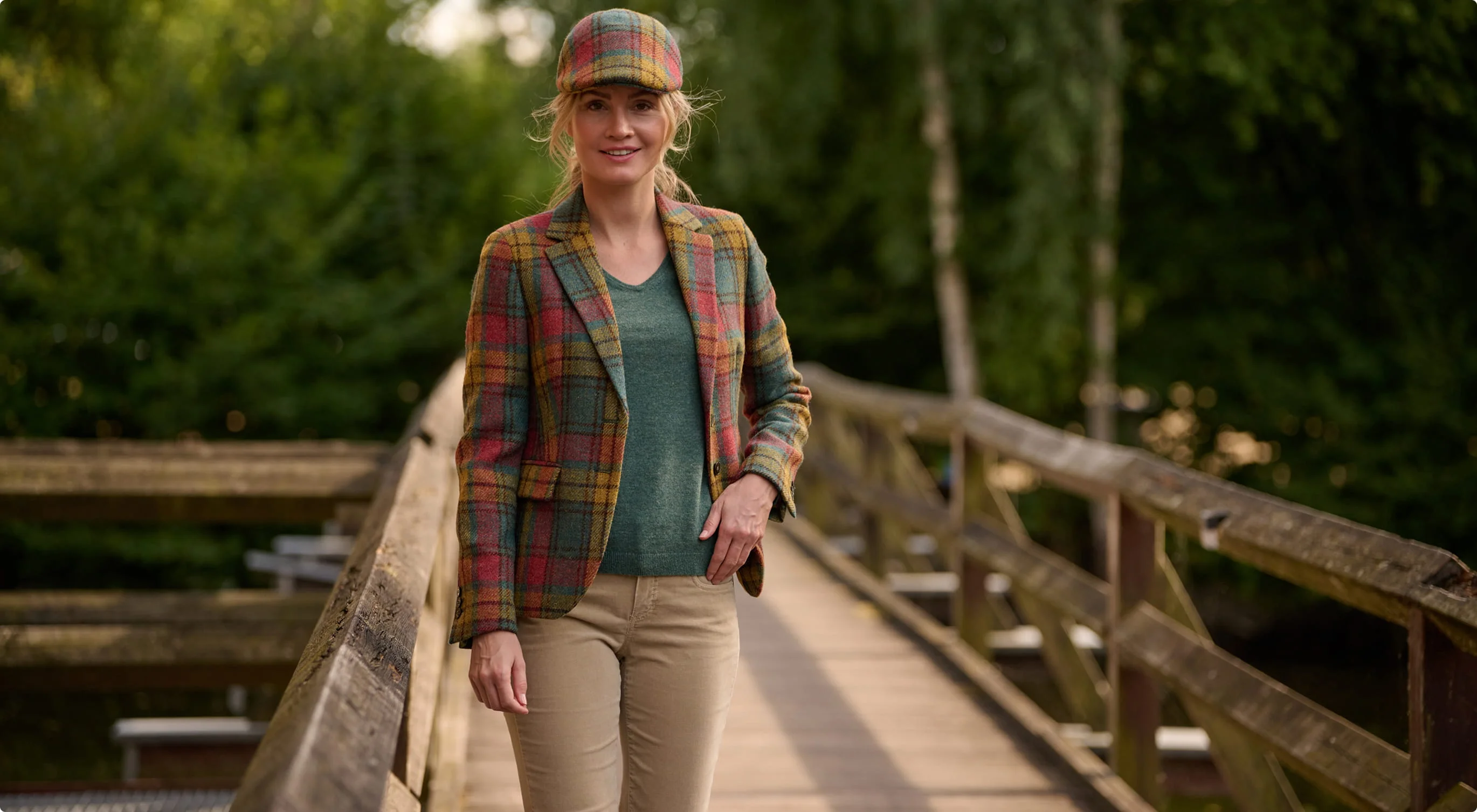 Woman in a checked tweed blazer and matching flat cap on a wooden footbridge.