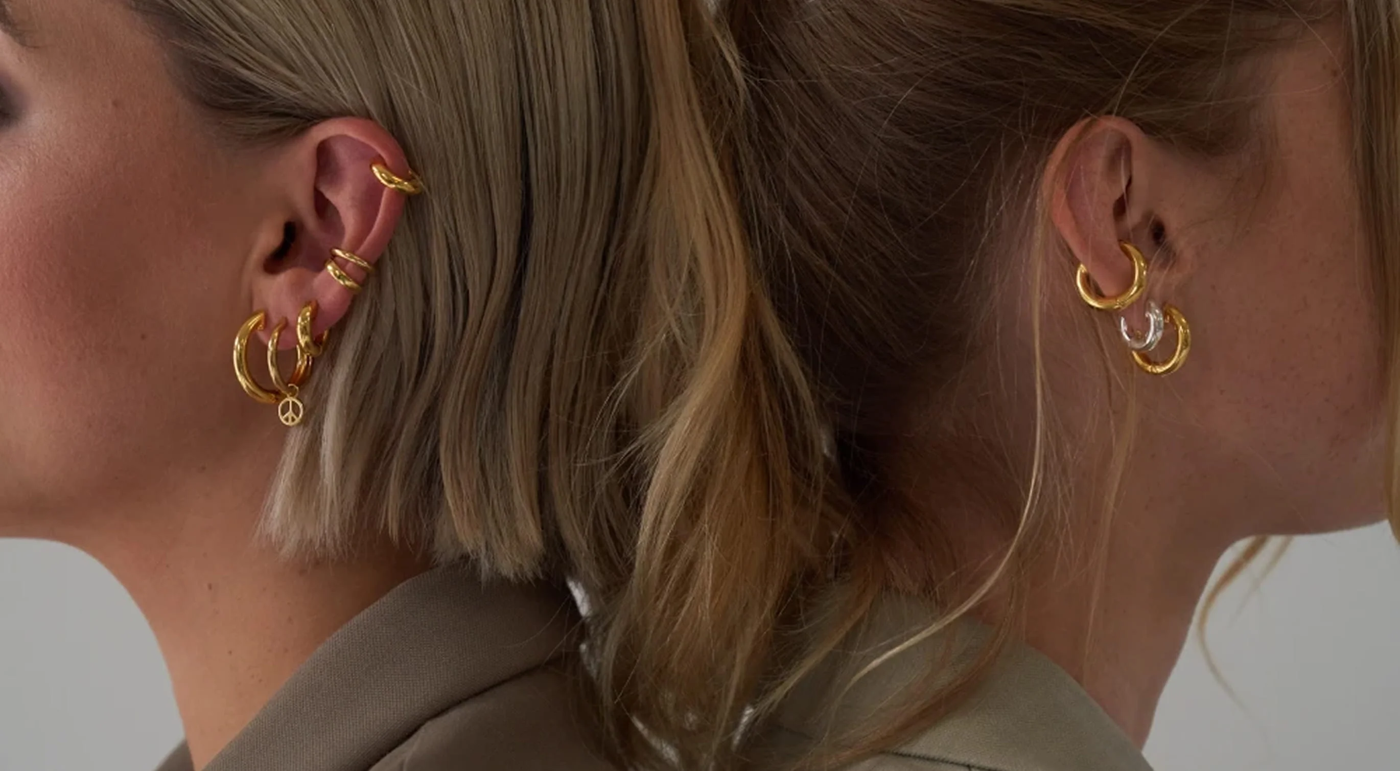 Two women back to back wearing gold hoop earrings and ear cuffs