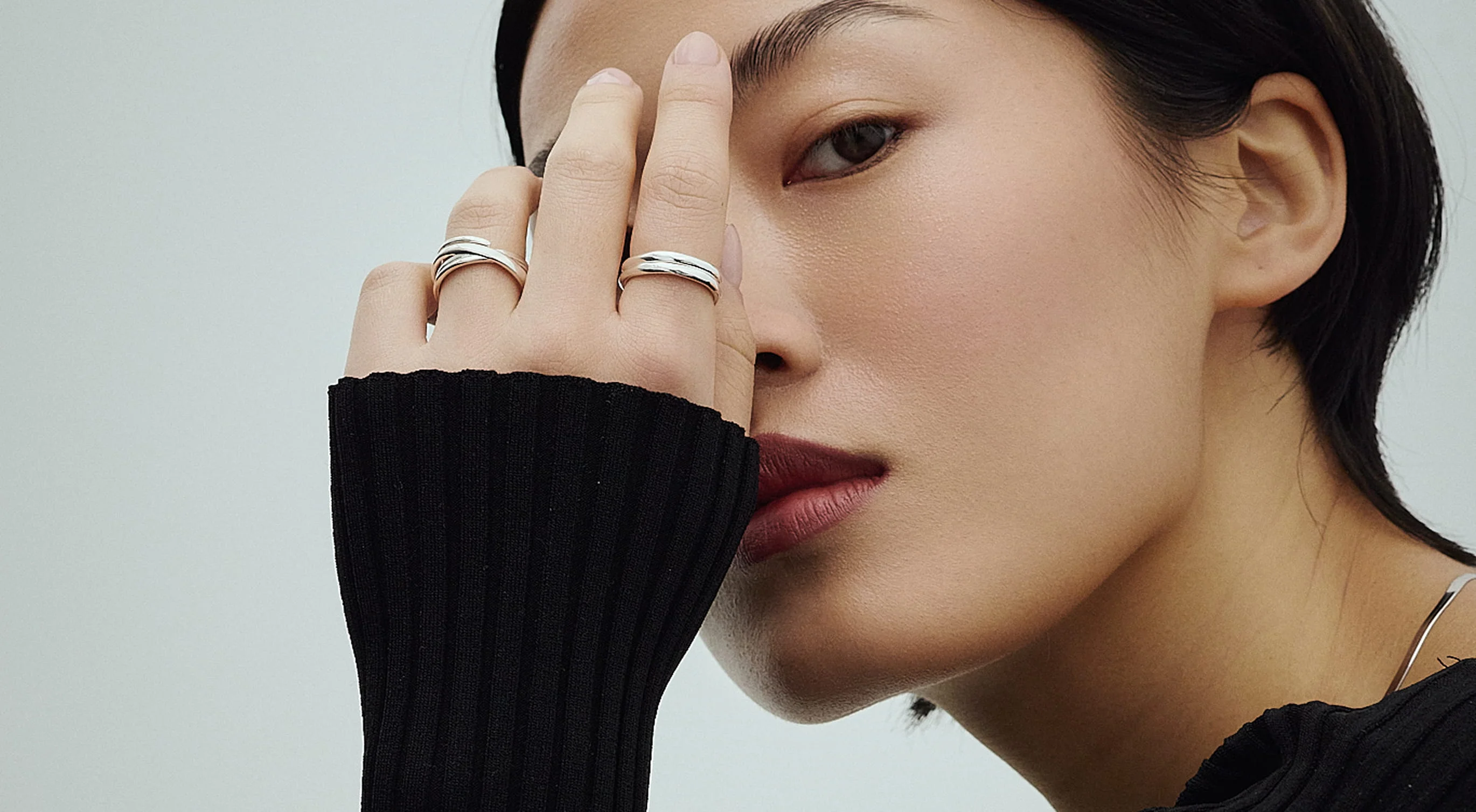 Woman in a black ribbed top with two silver rings, her hand raised to her face