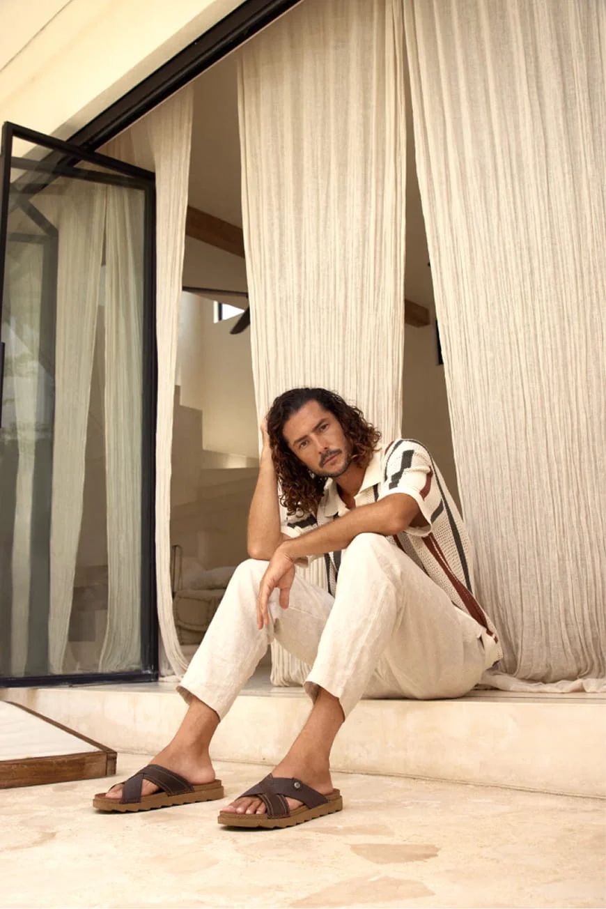 Man in linen trousers and a striped shirt sitting on steps.