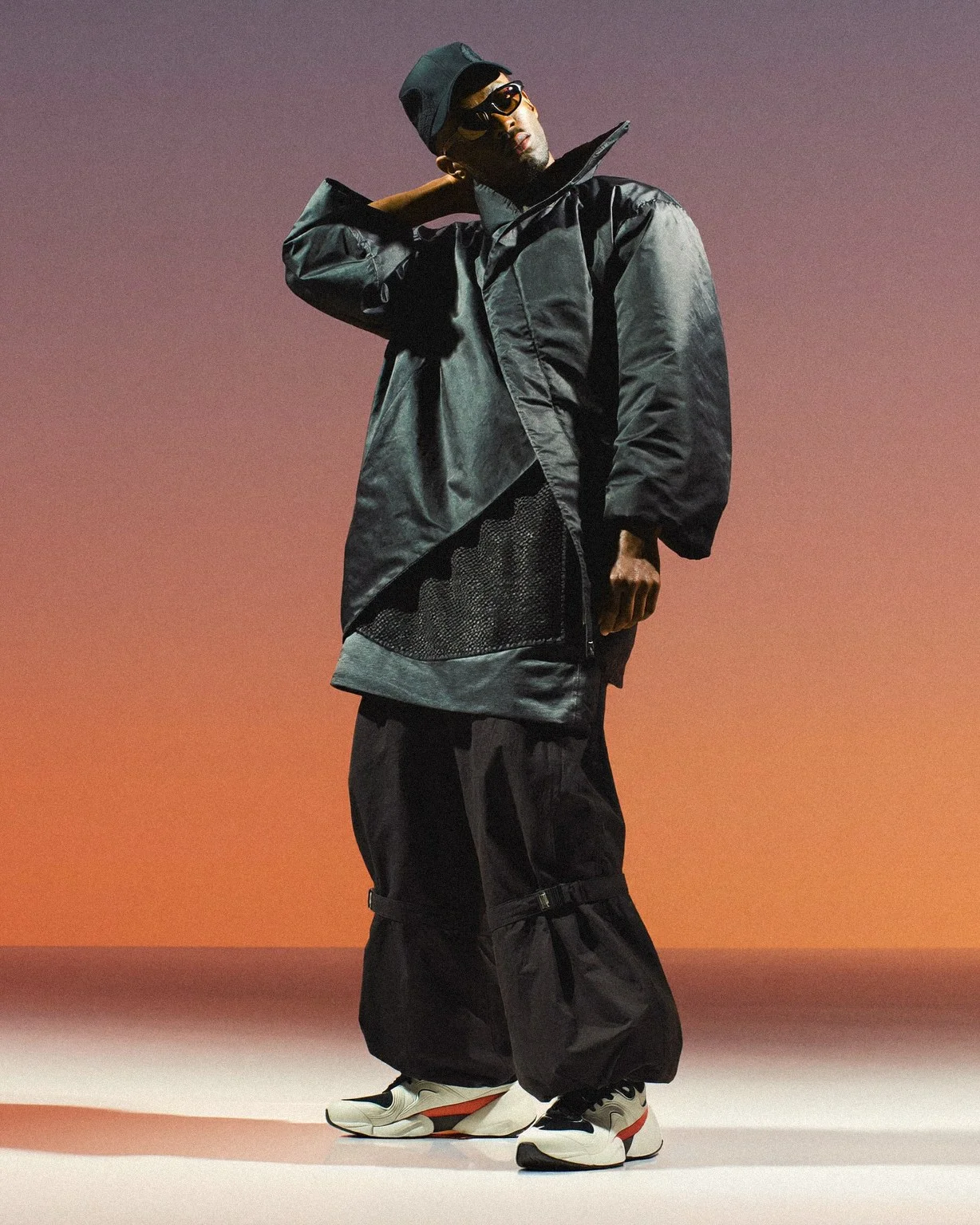 Model in an oversized grey jacket and black cargo trousers against an orange gradient