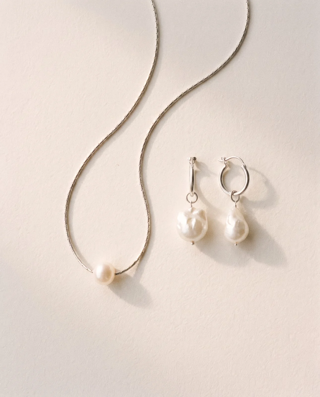 Pearl necklace and pearl earrings on a cream background