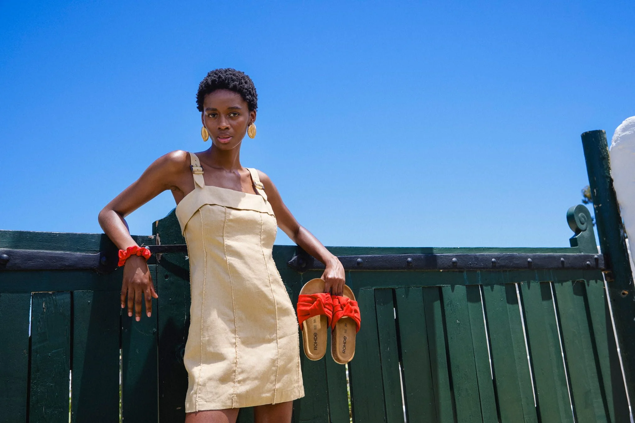 Woman in a tan dress holding red sandals.