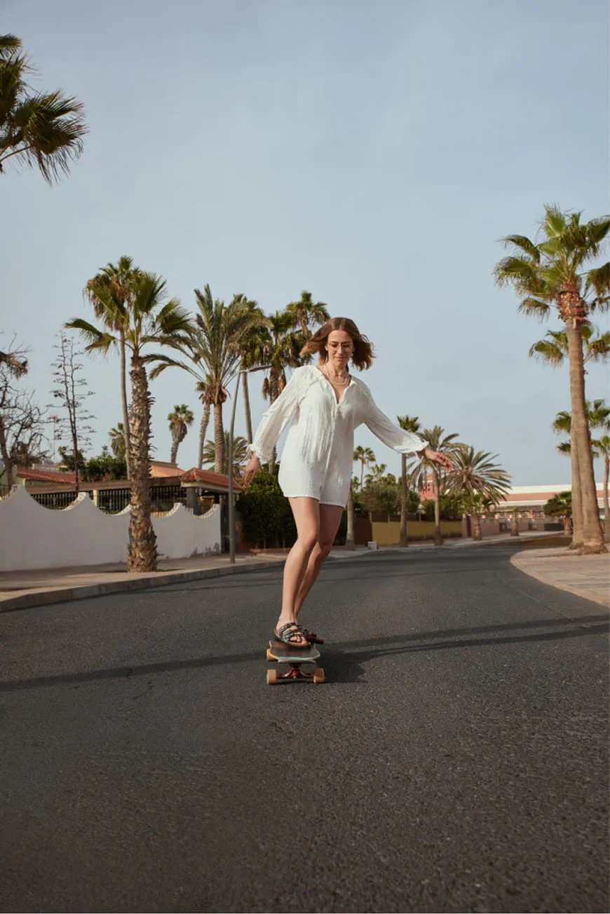 Woman skateboarding on a palm-lined road.