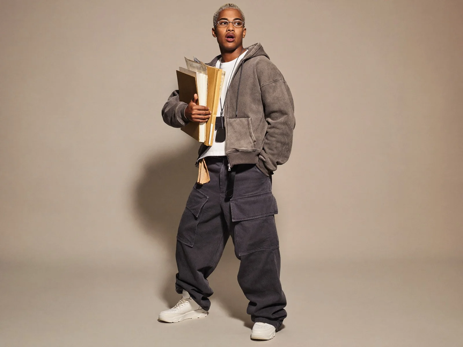 Man in a grey jacket and wide trousers against a beige studio backdrop