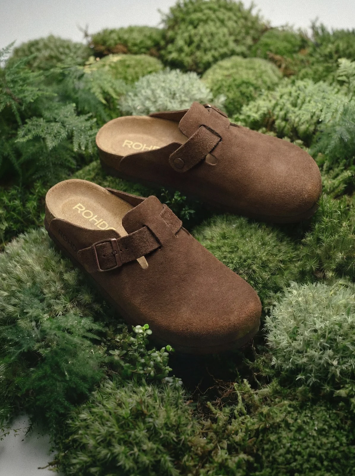 Brown suede clogs on a bed of moss
