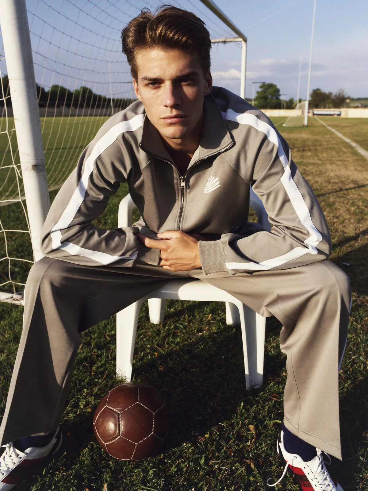 Man in a beige tracksuit sitting by a football goal