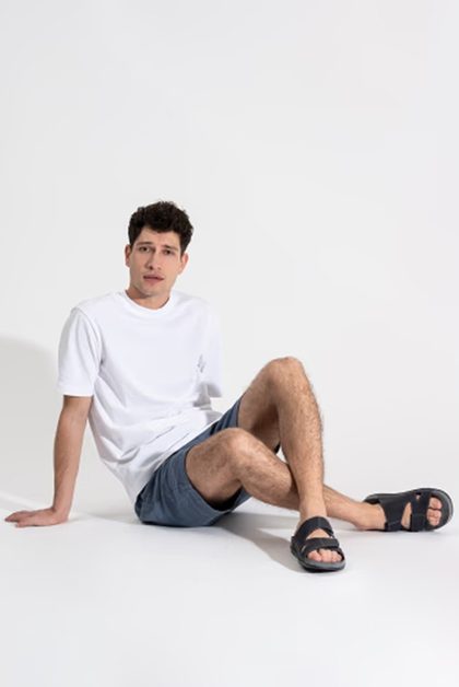 Man in white t-shirt, shorts and slides, seated