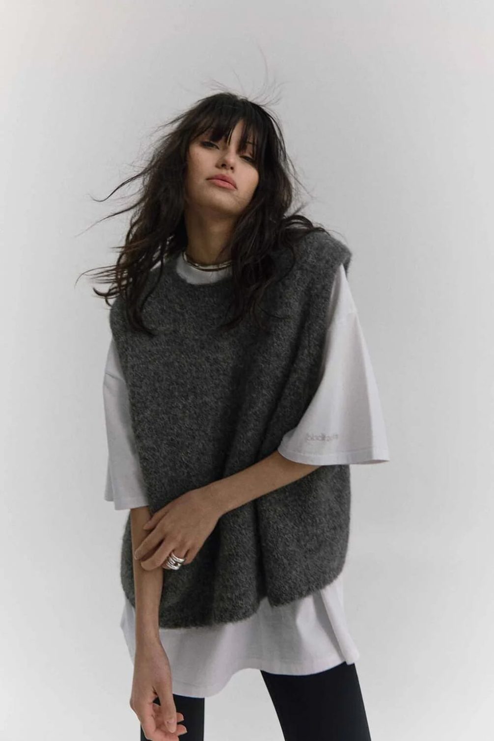 Fashion model wearing a grey knit vest over a white t-shirt.