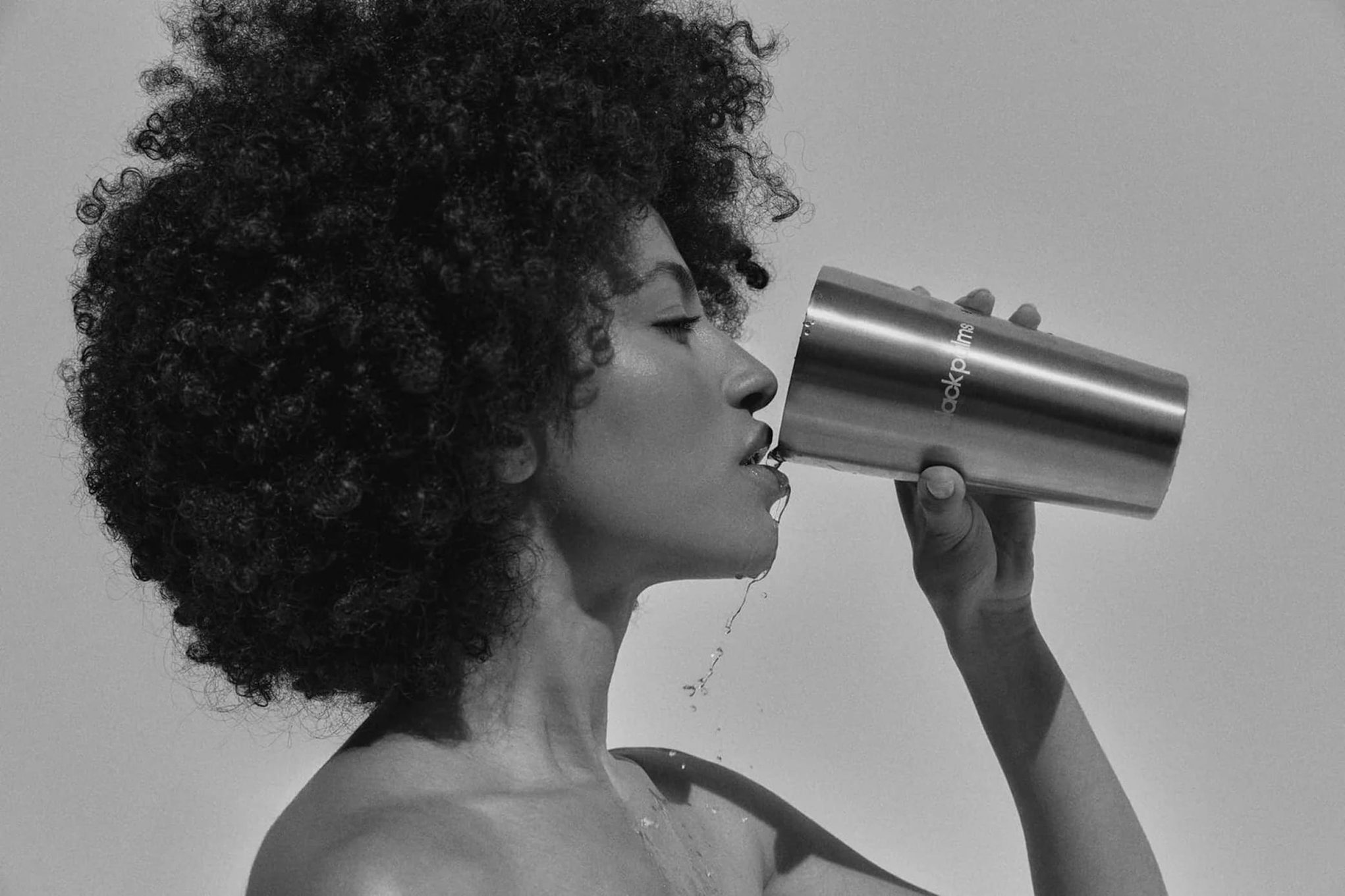 Woman with afro drinks from metal tumbler.