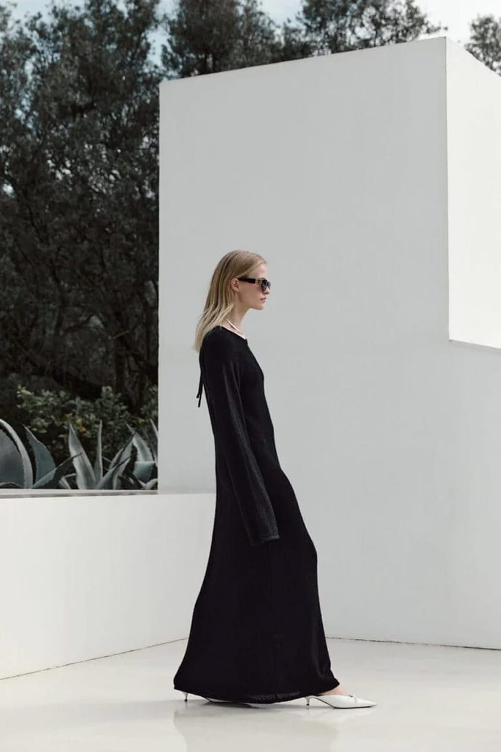 Model in black gown and sunglasses walking.