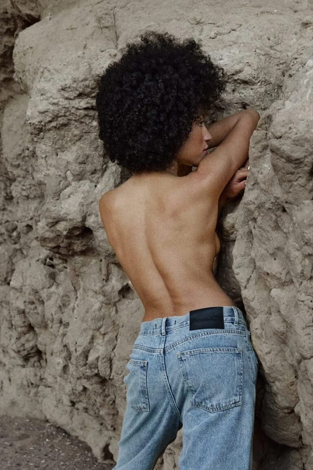 Fashion model in blue jeans against rock texture.