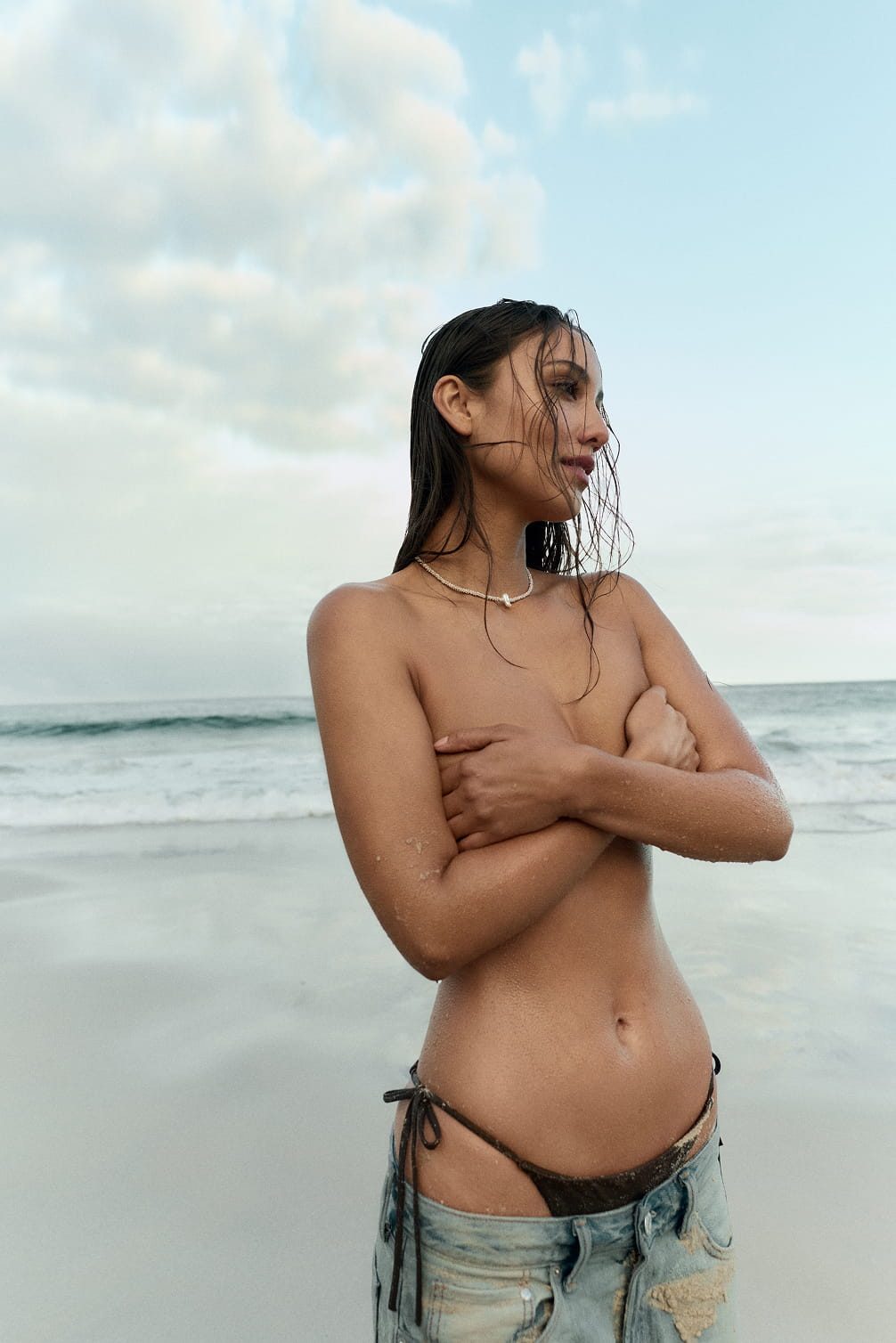 Woman with wet hair on a beach, hands covering chest.