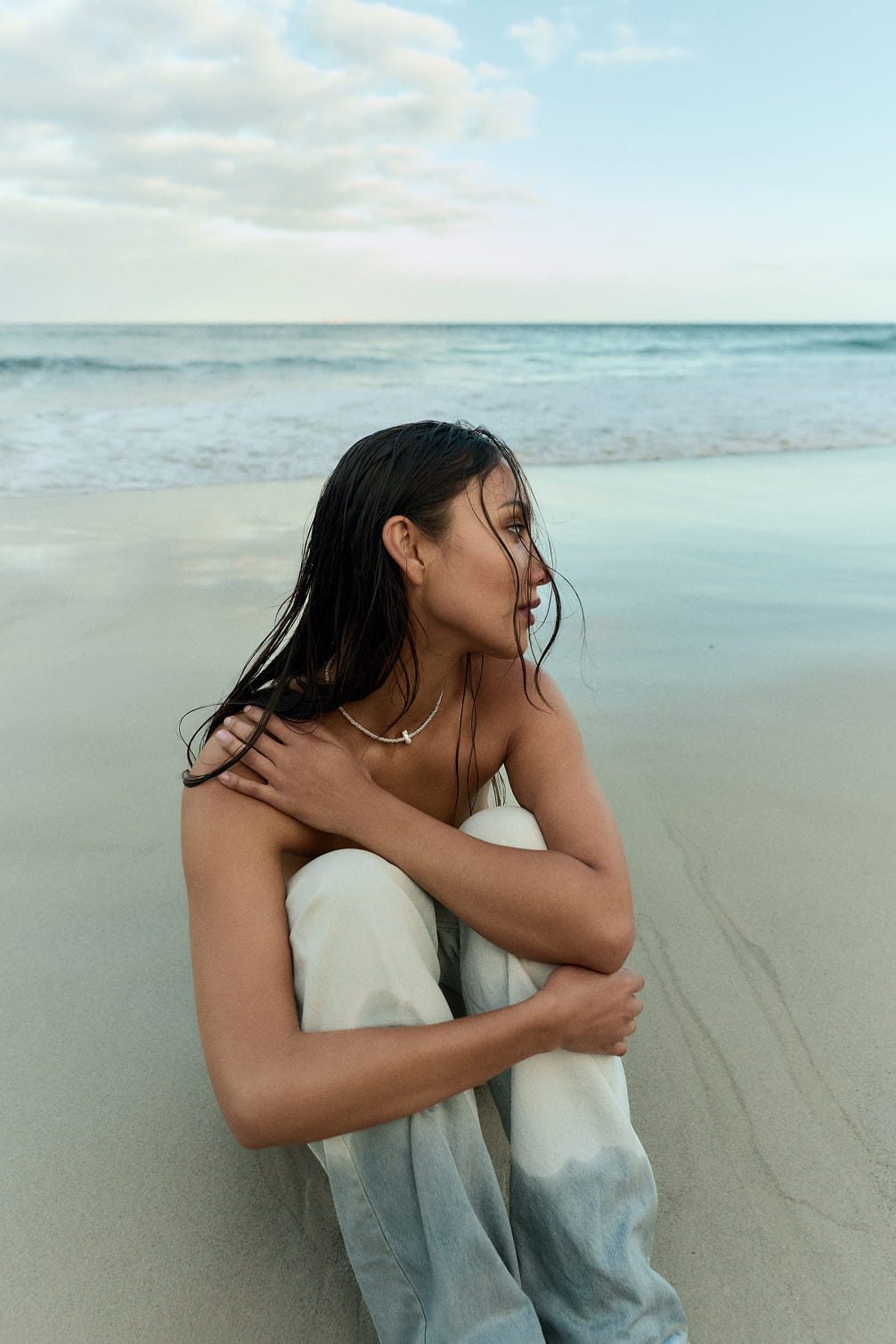Woman sitting on a beach with wet hair and jeans