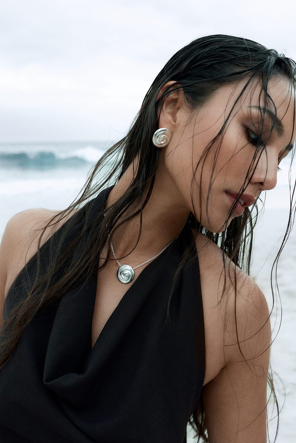Woman wearing silver spiral earrings and necklace outdoors.