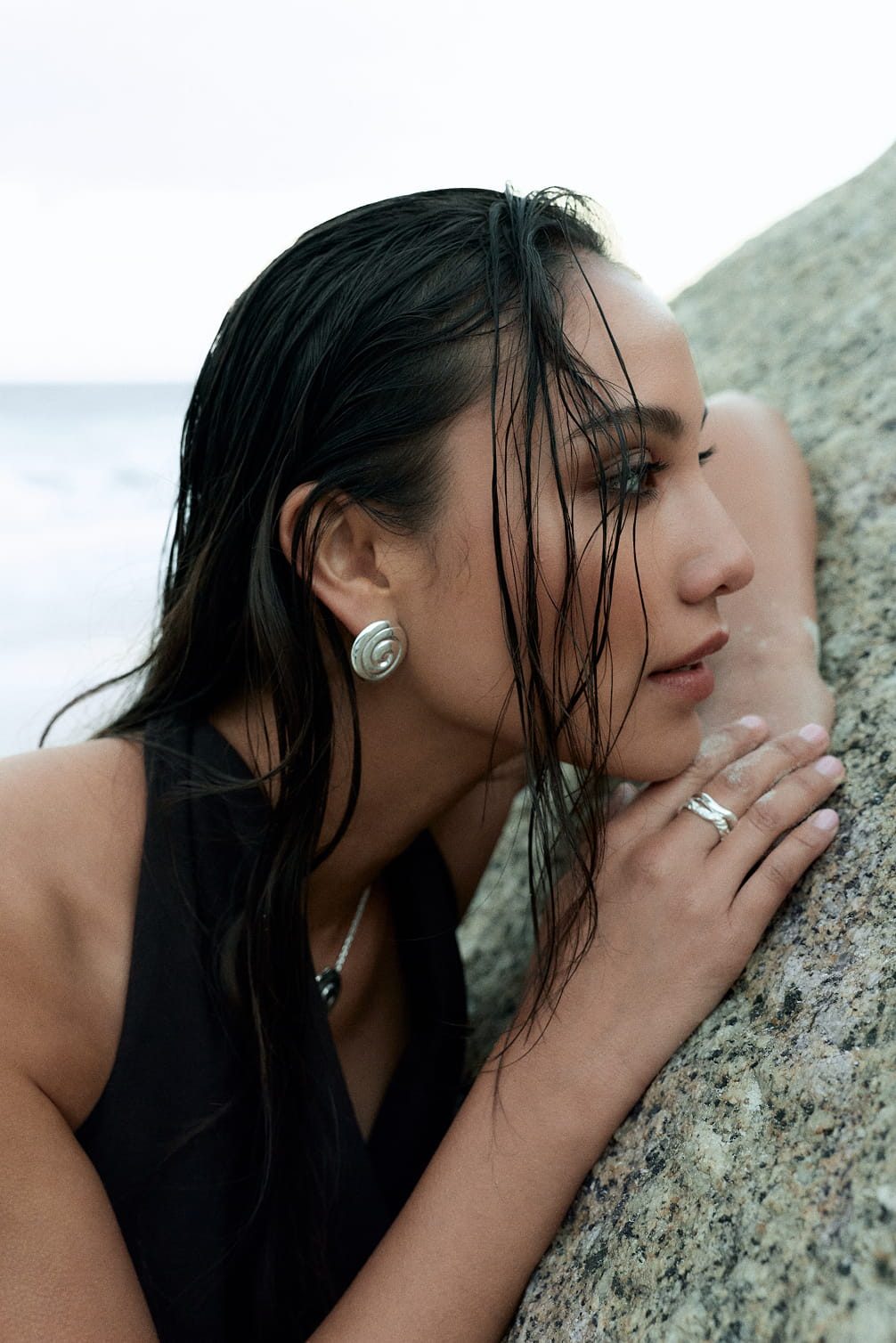 Woman with wet hair and jewelry rests on a rock.