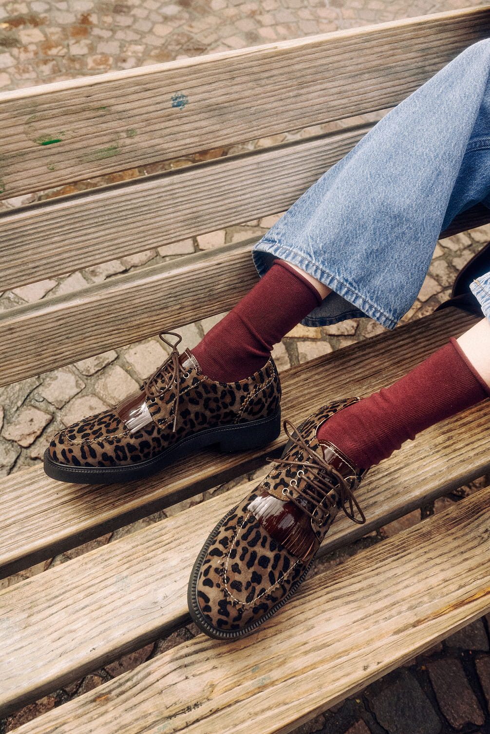 Leopard print loafers with burgundy socks on a bench.