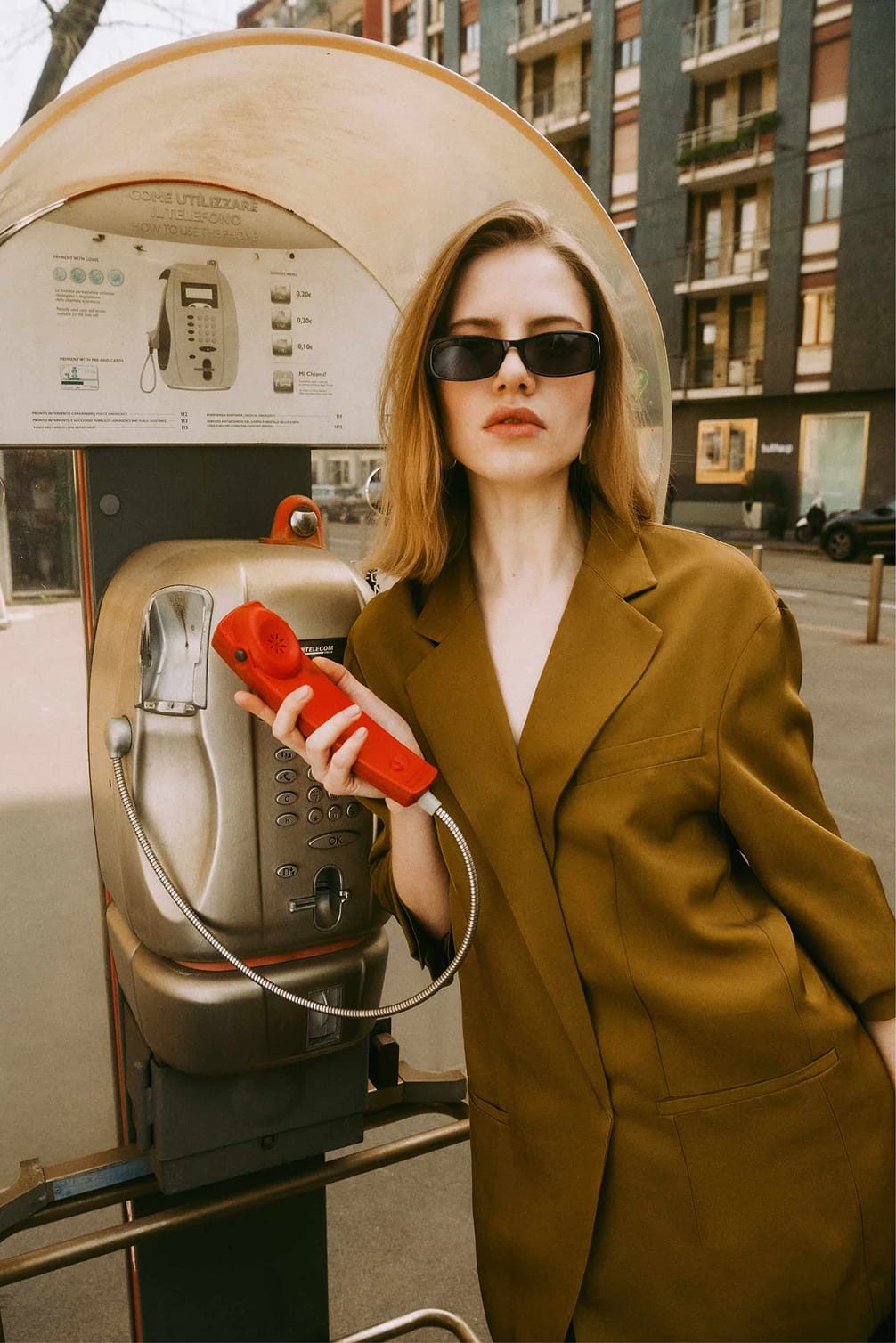 Woman in sunglasses holds an old red payphone receiver.