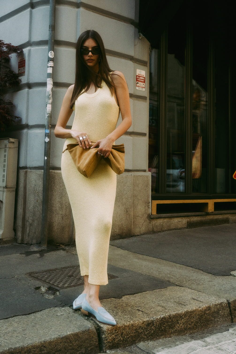 Woman in yellow dress and sunglasses holds clutch.