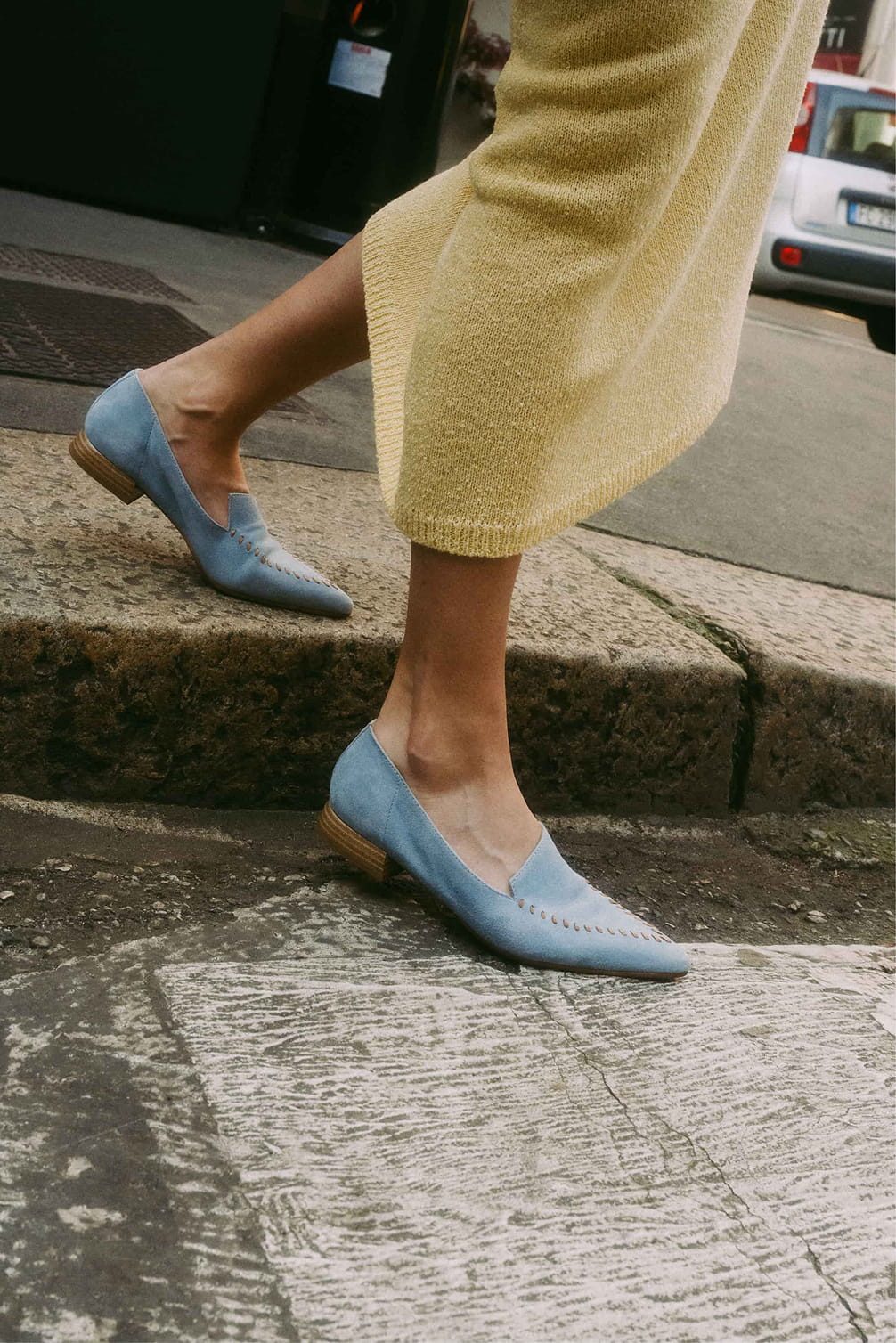 Blue suede loafers with a yellow skirt walking on steps.