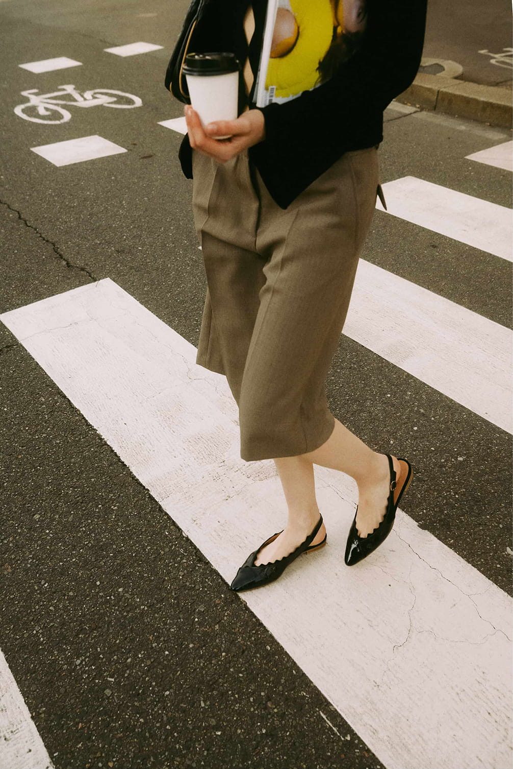 Person crossing street on a zebra crossing with coffee cup.