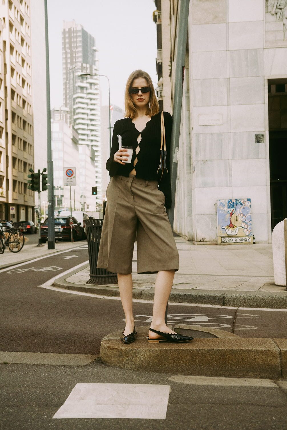 Woman in black cardigan and culottes holding drink.