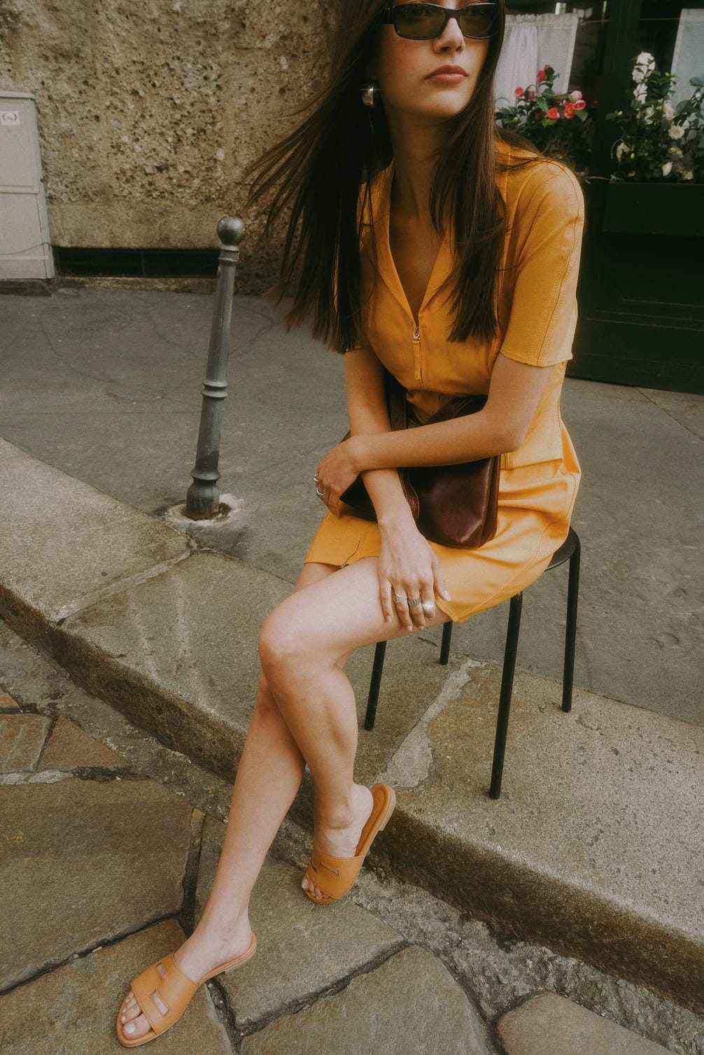 Woman in orange dress and tan sandals sitting on stool.