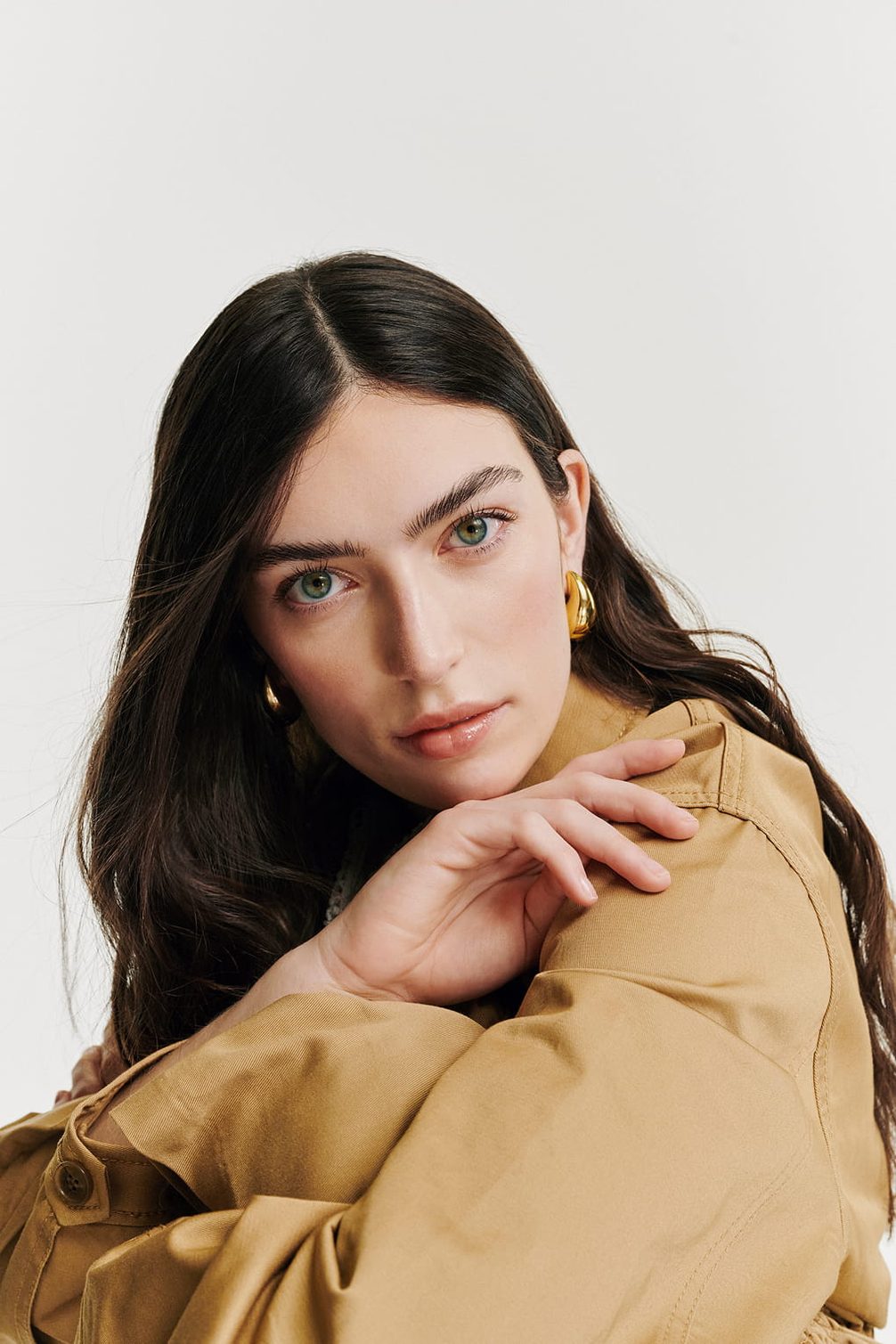 Model with tan jacket and gold earrings