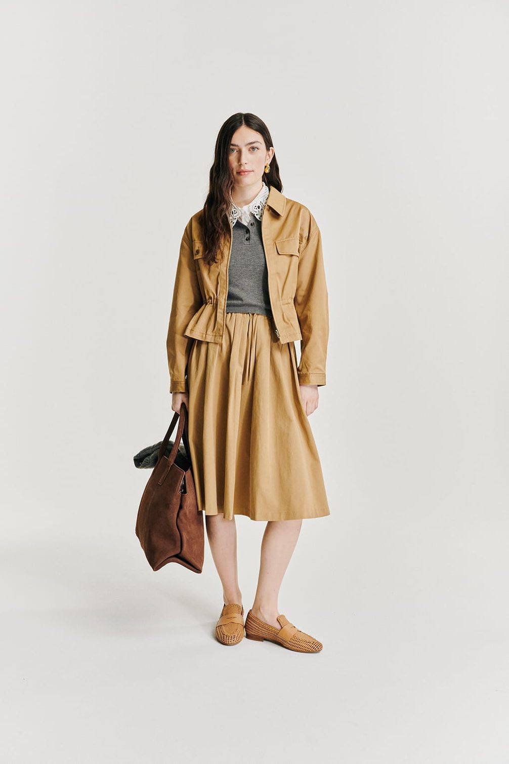 Model in tan jacket, grey sweater, tan skirt, loafers, tote