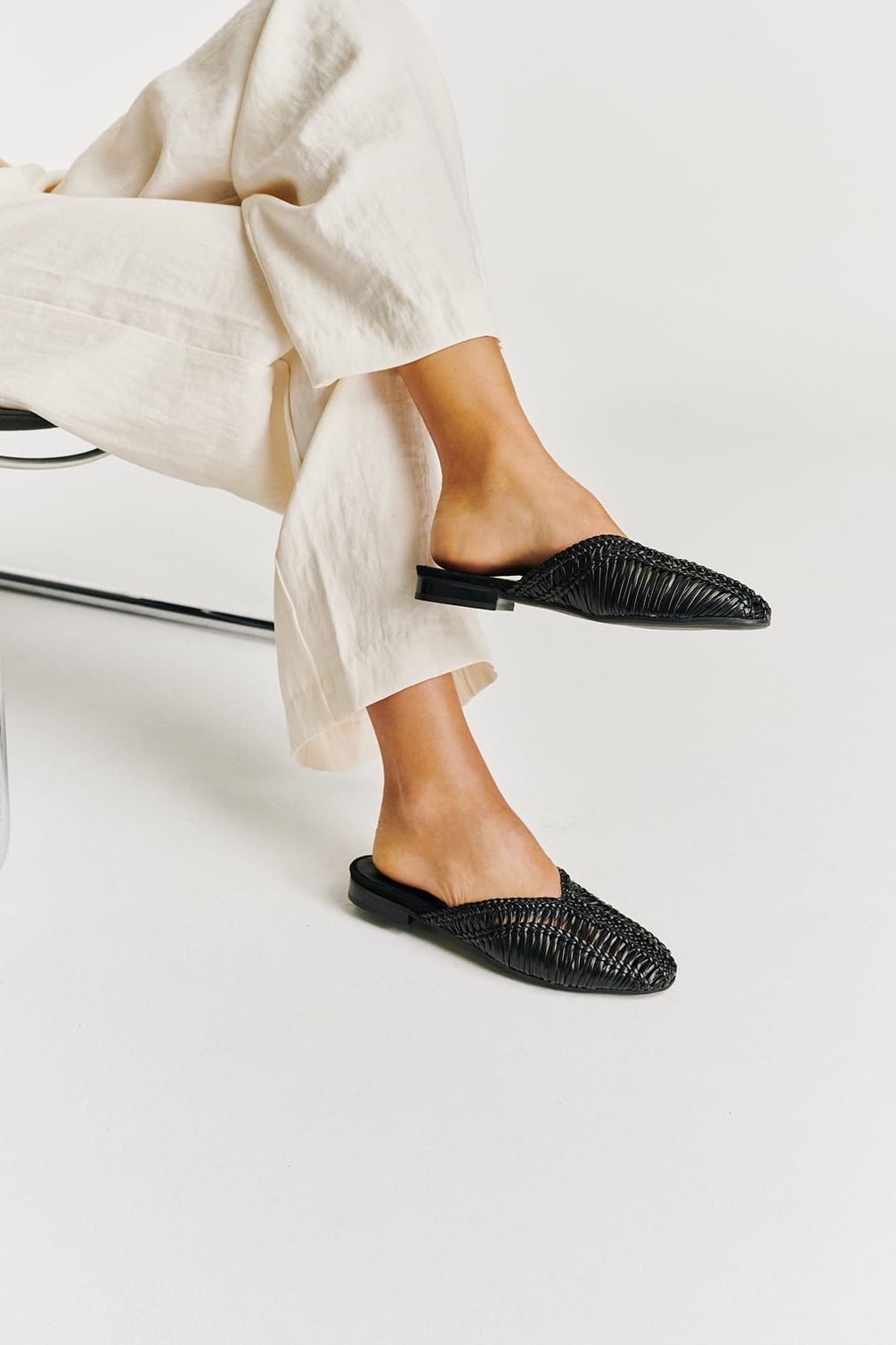 Woven black mules on feet.