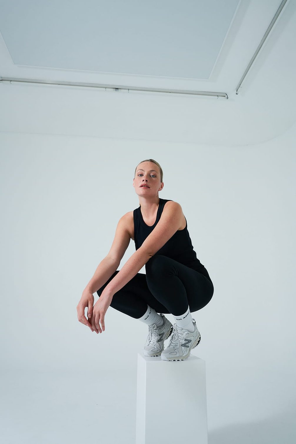 Woman in black activewear and sneakers squats.