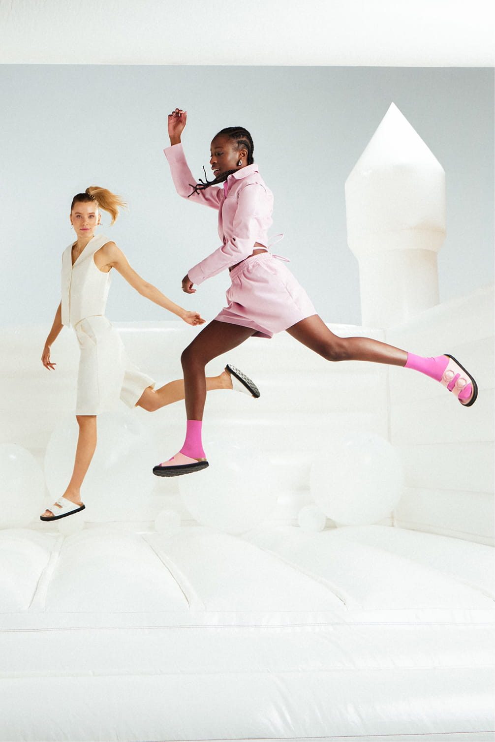 Two models jumping in a bouncy house with pink and white outfits.
