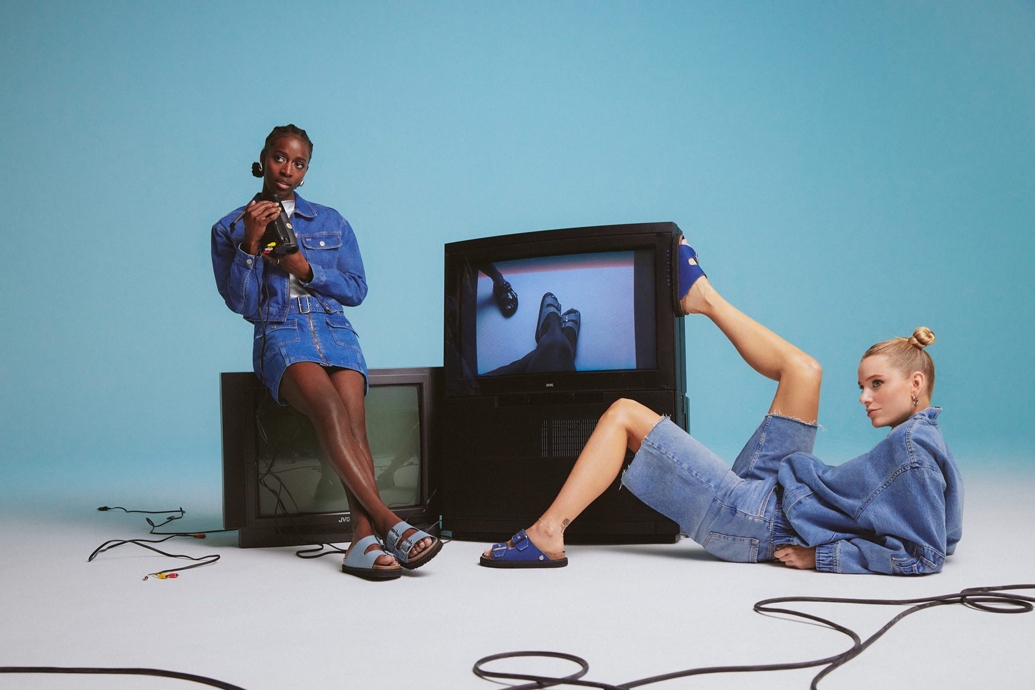Two women in denim outfits near vintage TVs.
